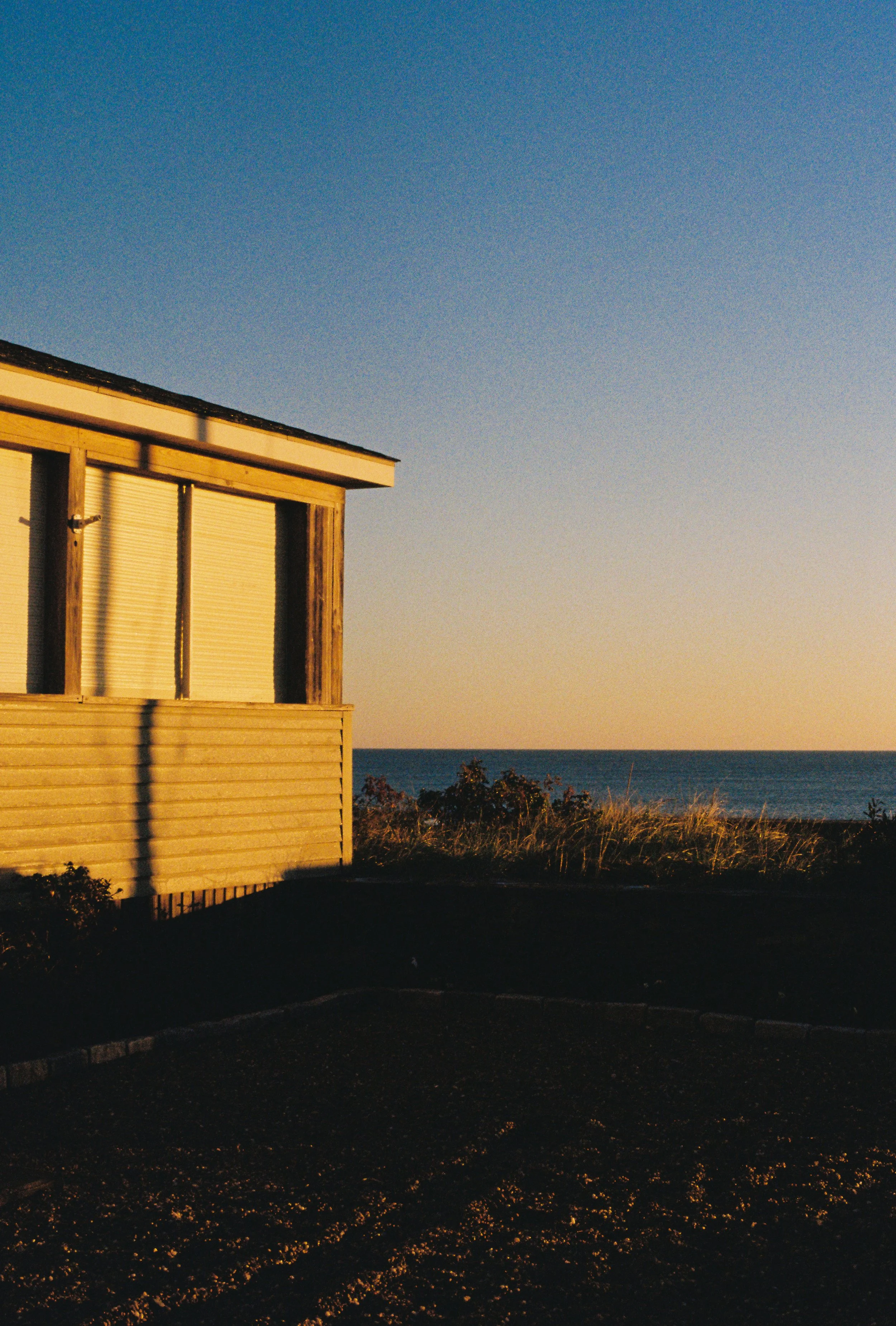 A wooden house near the coast with a view of the ocean and a clear sky at sunrise.