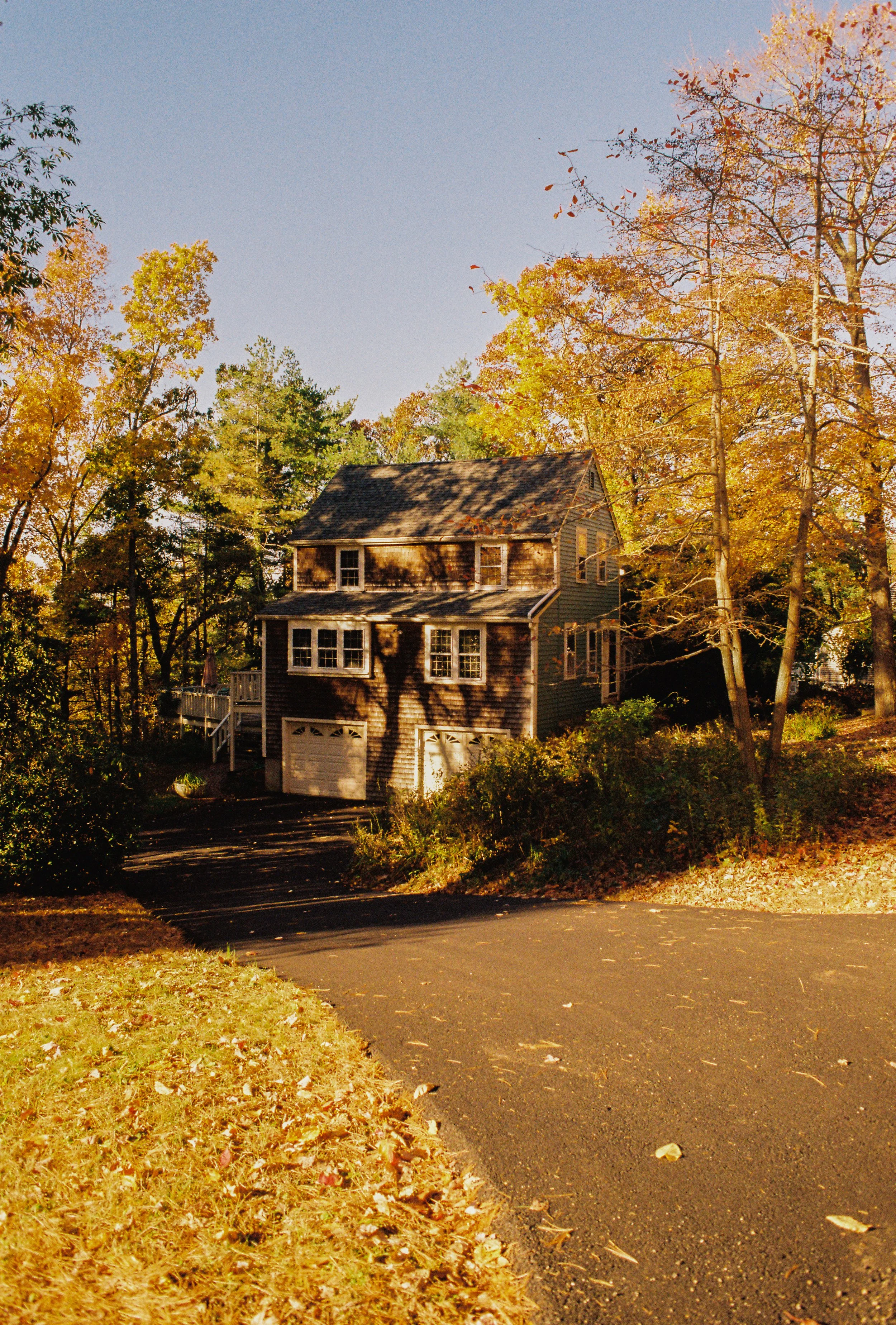 A two-story house with a garage, surrounded by trees with autumn-colored leaves, under a clear sky.