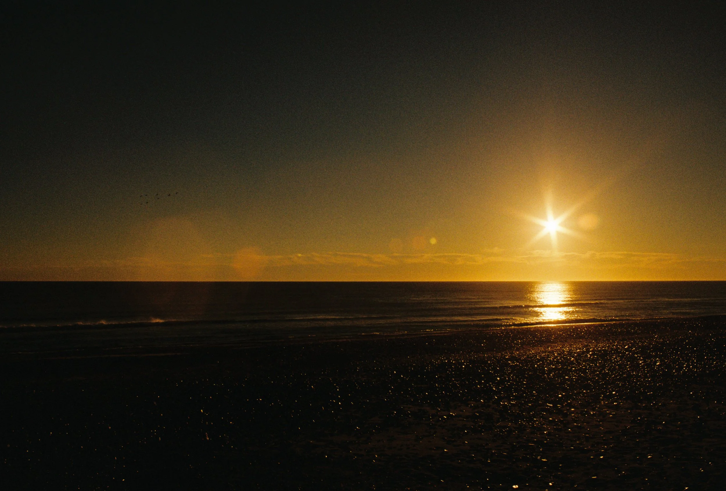 Sunset over the ocean with a dark sky and reflection on the water, view from the beach