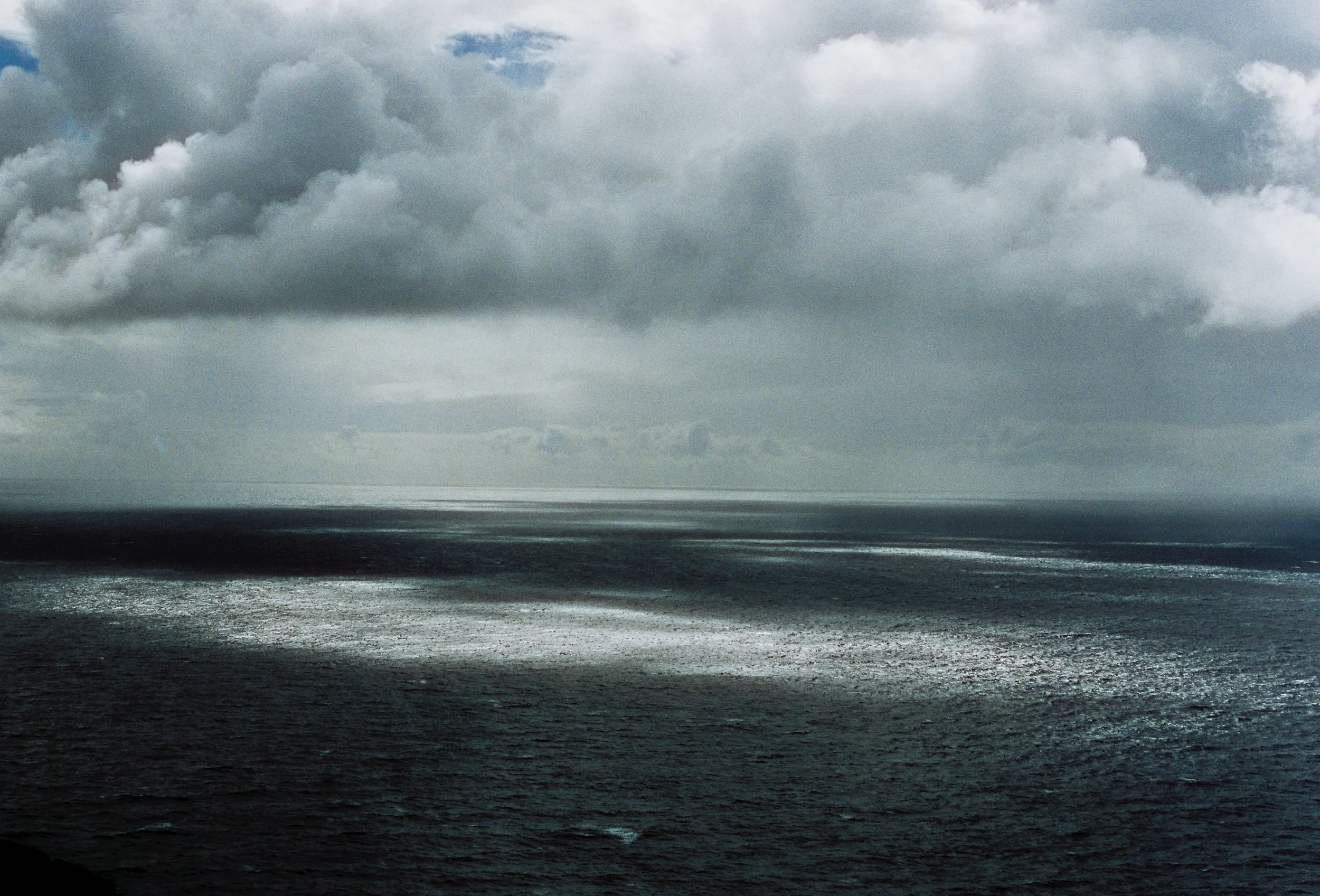 Overcast sky with dark clouds above the ocean, with some lighter patches reflecting on the water surface.