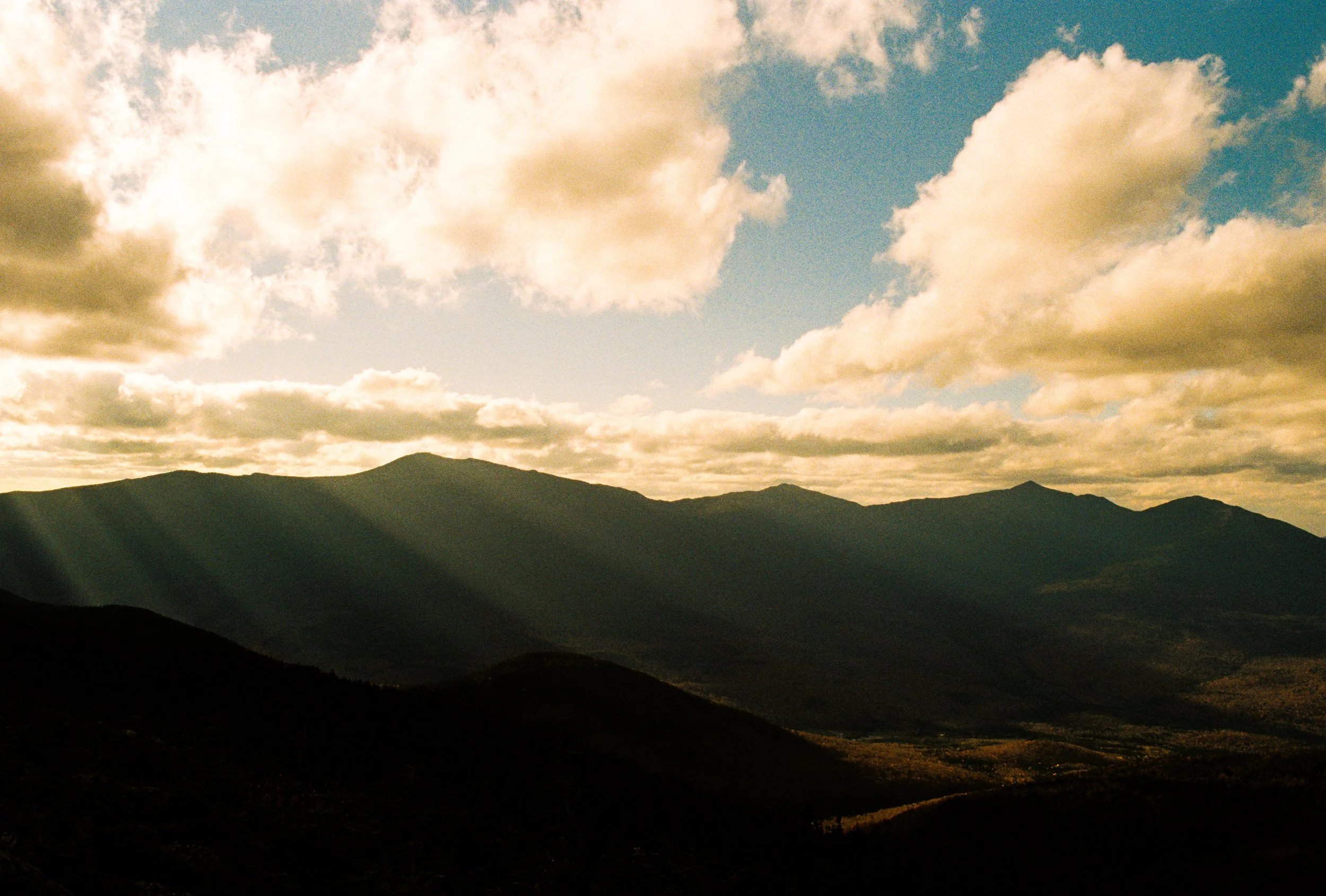 Sunlight streams through clouds over a mountain range with layered peaks