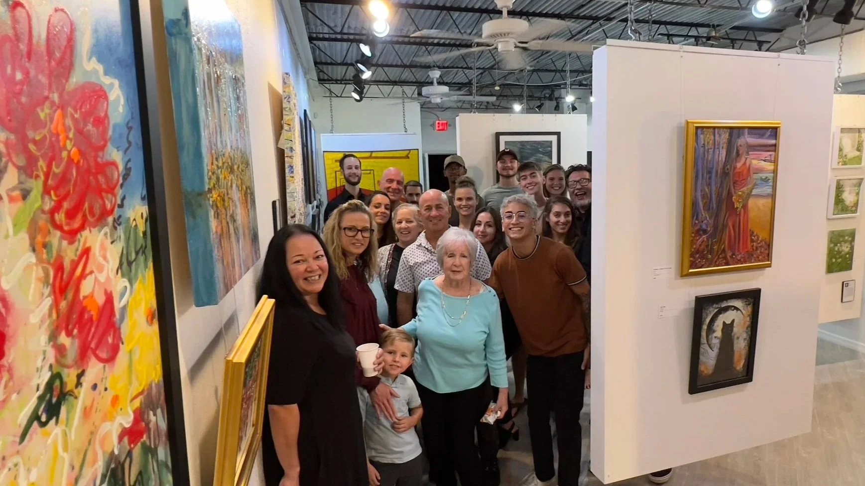 A group of people at an art gallery, standing in front of colorful paintings, smiling and posing for the photo.