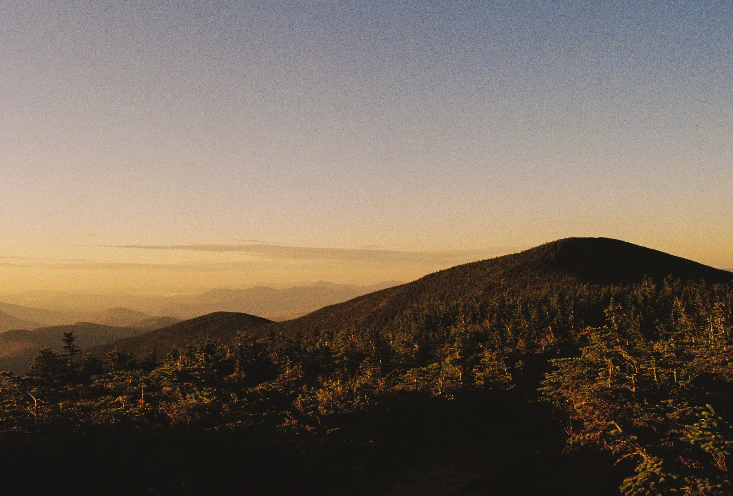 Sunset over a mountain landscape with a dense forest in the foreground.
