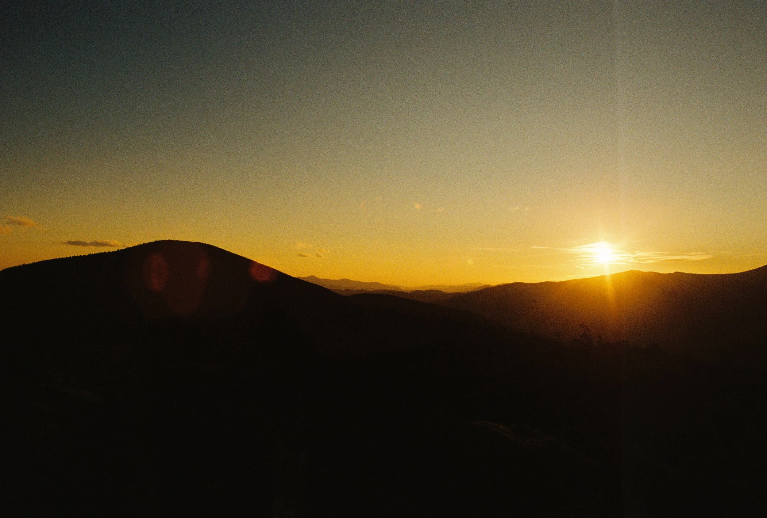 Sunset over a mountain landscape with a clear sky and a few scattered clouds.