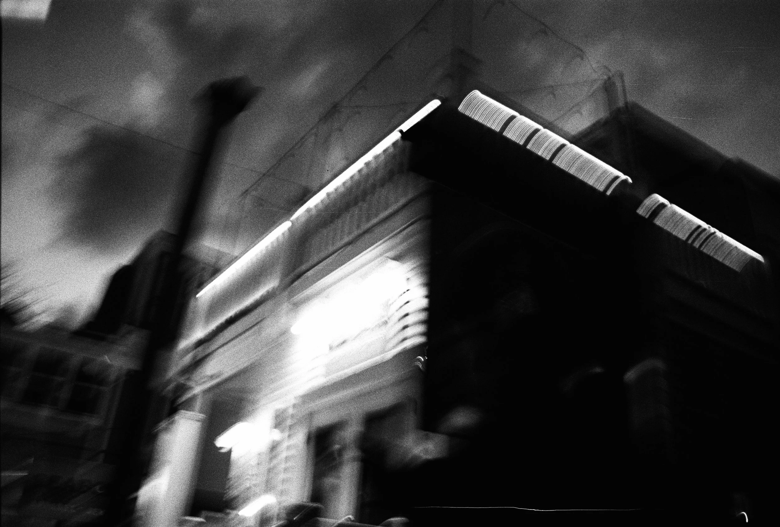 Blurry black and white photo of a building exterior at night, with illuminated details and possibly a chimney or other tall structure on the roof.