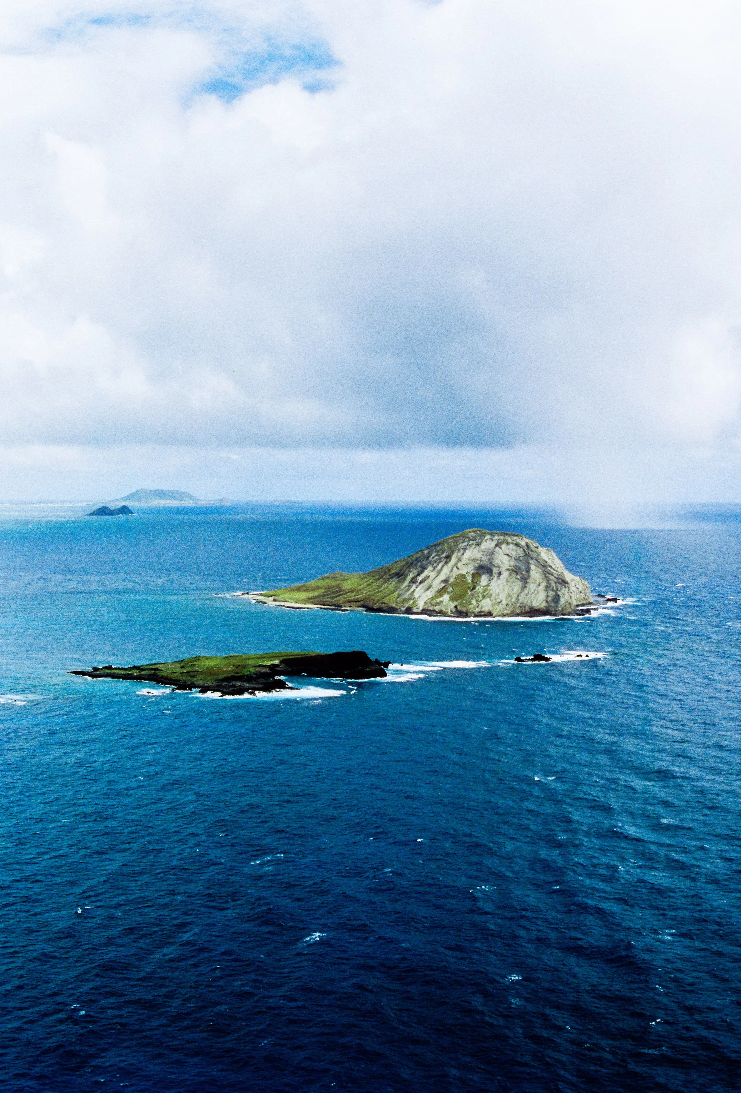 Aerial view of three islands in the ocean, with one large island and two smaller ones, under a partly cloudy sky.