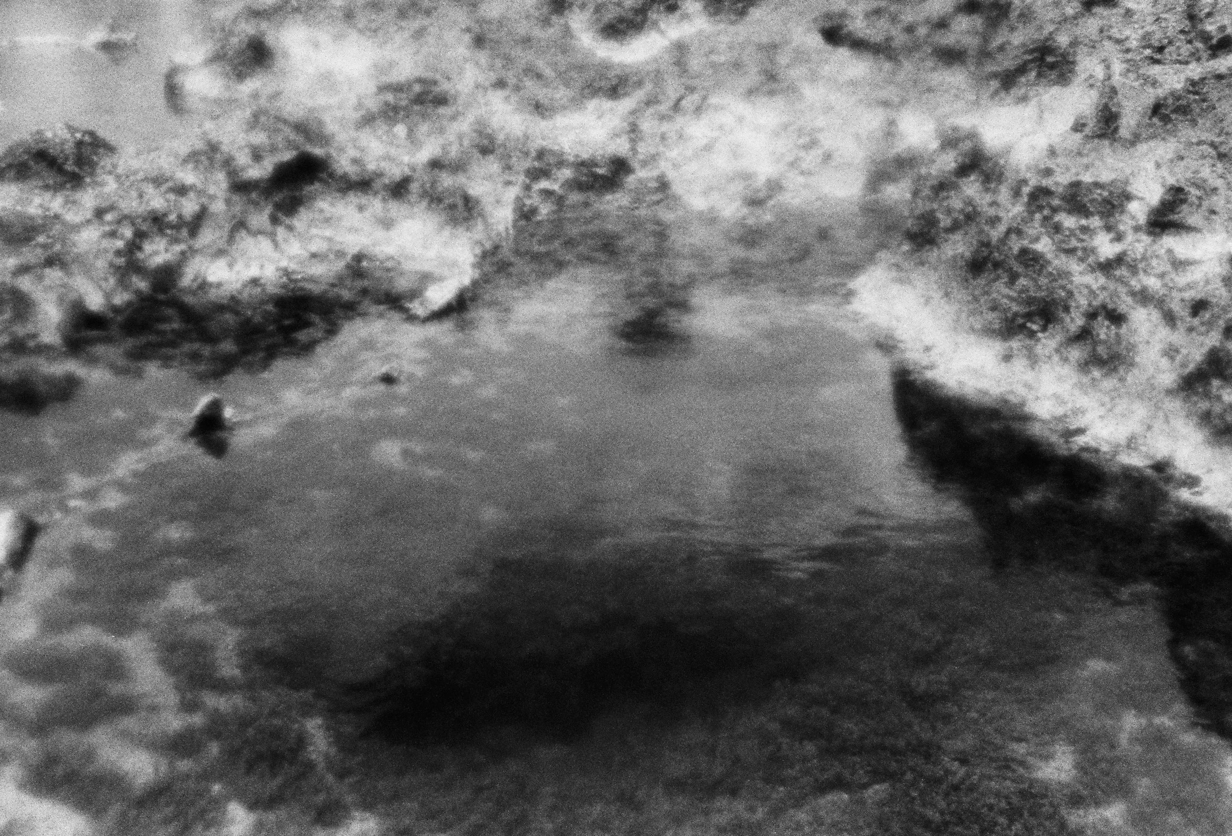 A close-up black and white photograph of a dry rock formation in Hawaii and a tidal bay of water.