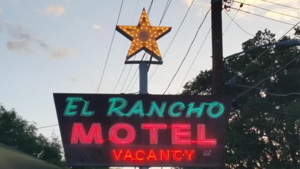Neon sign for El Rancho Motel  in Bishop Ca. with a large illuminated star above, and a clear sky in the background.