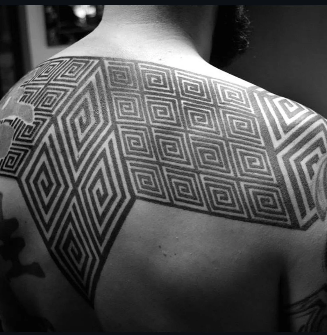 Geometrisches schwarzes Tattoo mit wiederholten Spiralen über Schultern und oberem Rücken