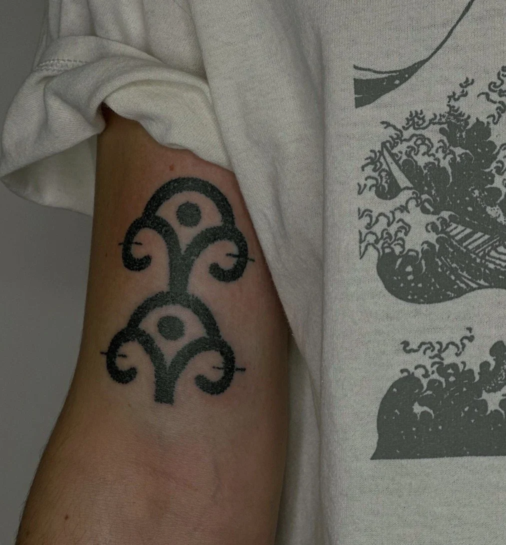 Small black ornamental tattoo on the upper arm.