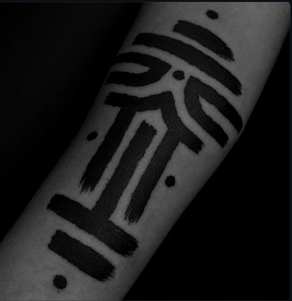 Bold black ornamental tattoo with brushlike lines on the forearm.