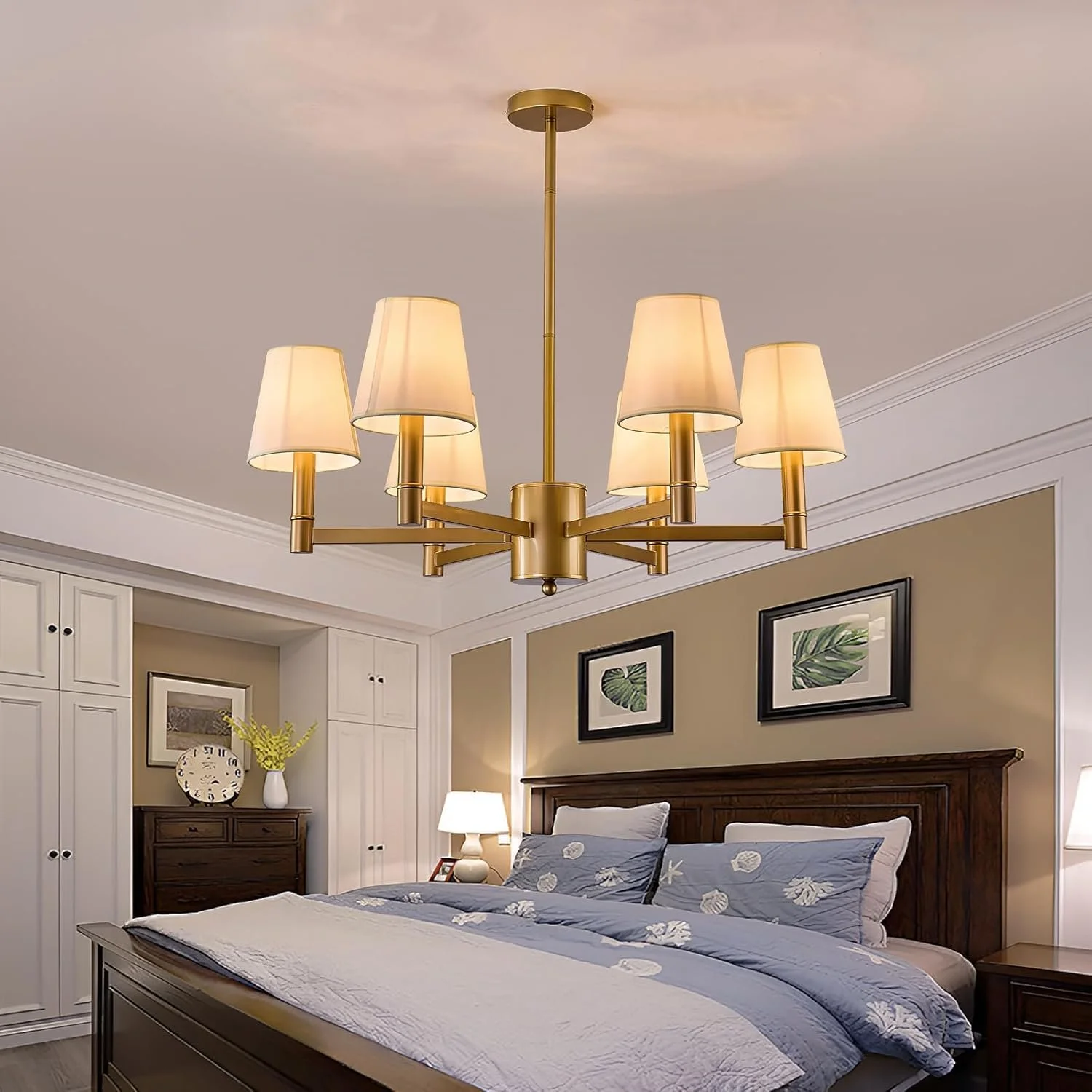 A bedroom with a brass chandelier hanging from the ceiling, a wooden bed with seashell and starfish patterned blue bedding, and framed leaf artwork on the wall.