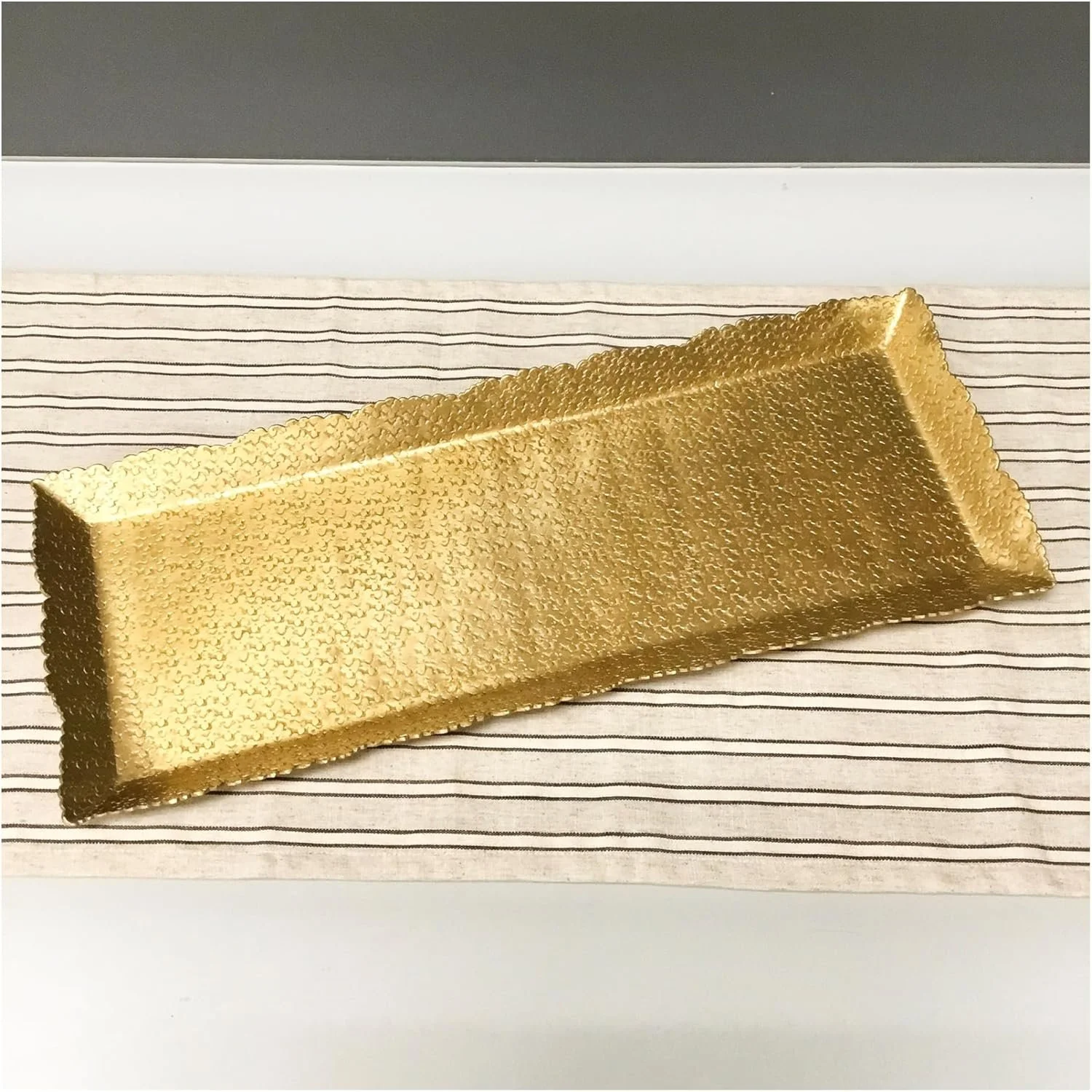 A rectangular sheet of gold-colored metal mesh placed on a striped cloth surface.