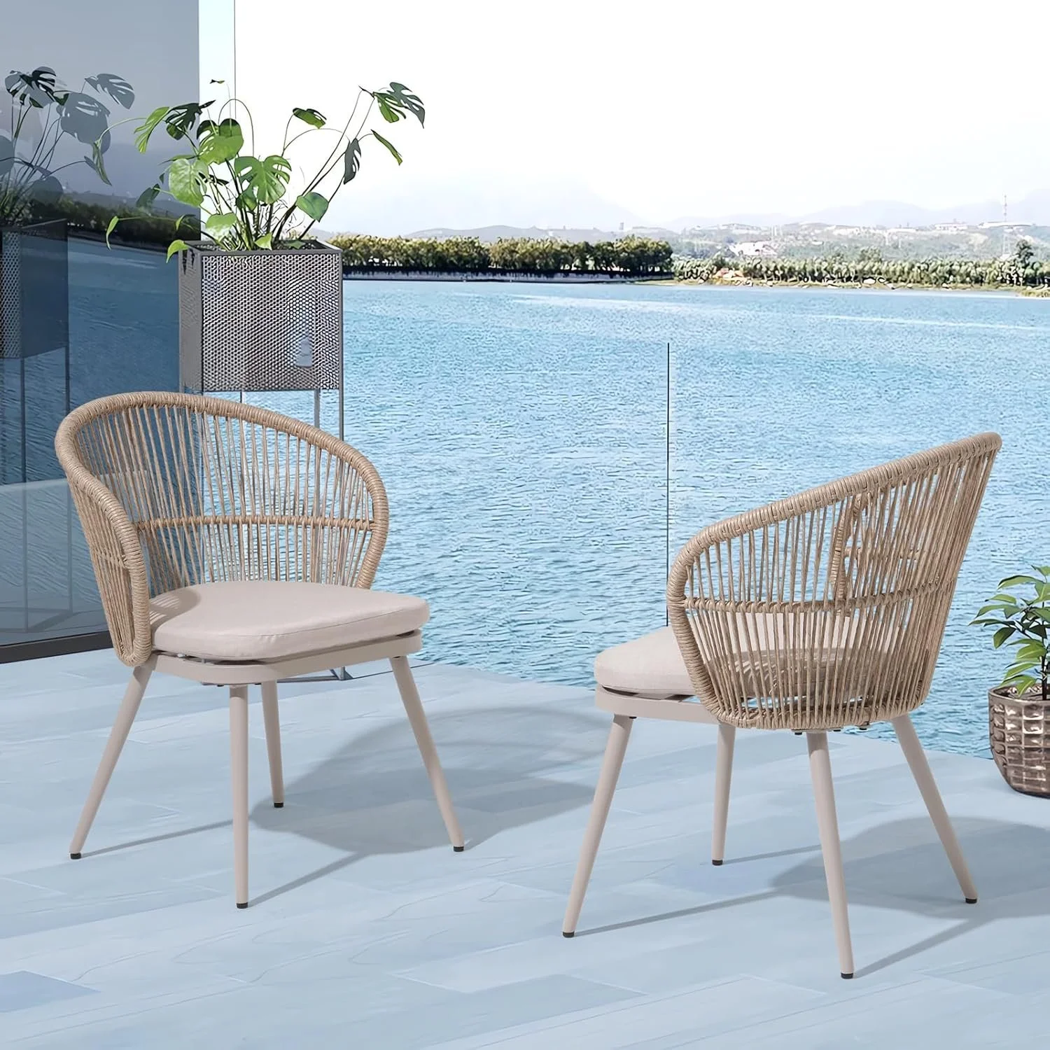 Two beige outdoor chairs with pillows on a balcony overlooking a body of water with trees and mountains in the distance.