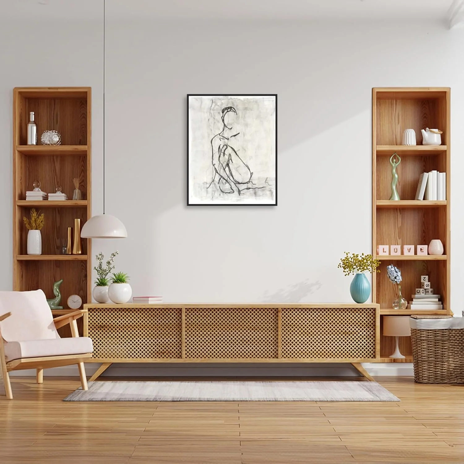 A modern living room with a white wall, two wooden shelves with decorative items, and a low wooden cabinet with a woven front. There are vases with plants on the cabinet and shelves, a framed line art drawing on the wall, a white armchair with wooden legs on the left, and a wicker basket on the right. A gray rug is on the wooden floor.