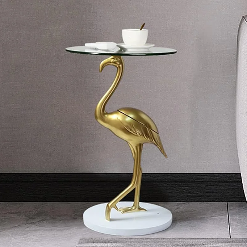 A decorative side table in the shape of a gold flamingo with a glass top, holding a white bowl and a cup.