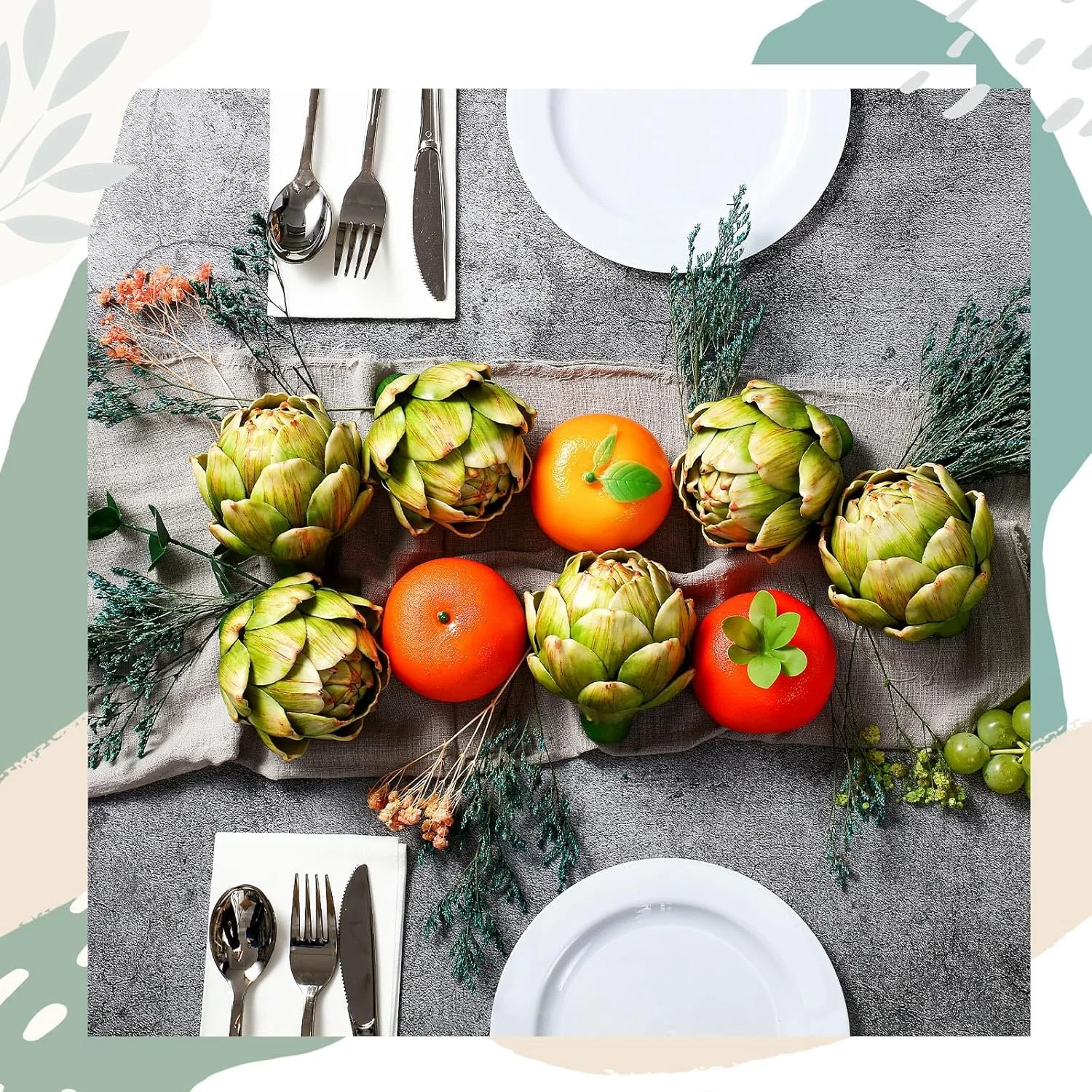 A table setting with a centerpiece of artichokes, orange fruits, and greenery on a gray tablecloth, surrounded by white plates and silverware.