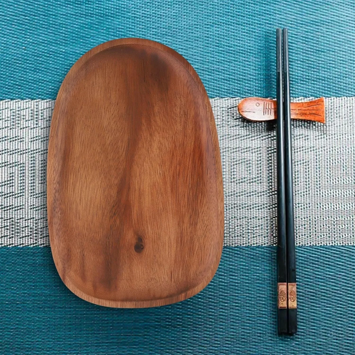Empty wooden plate with a pair of black chopsticks and a fish-shaped chopstick rest on a woven mat.
