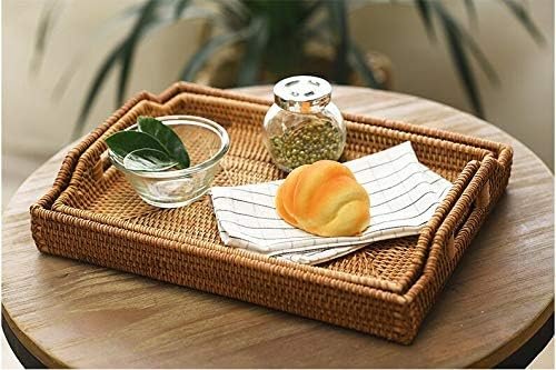 A wicker tray on a wooden table holding a glass bowl with two green leaves, a jar of mustard, a bread roll on a striped napkin, with plants blurred in the background.