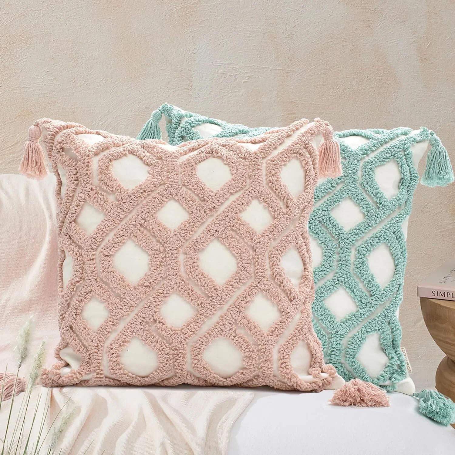 Two decorative pillows with pink and aqua tassels and textured woven patterns on a bed with light-colored bedding.