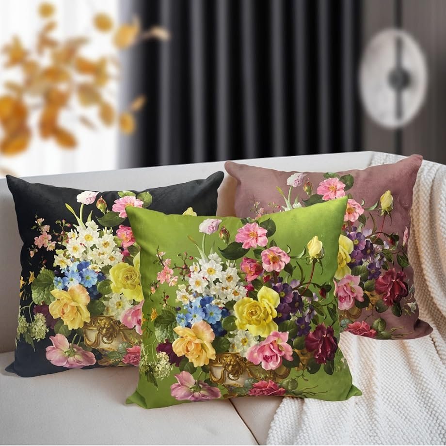 Four decorative pillows with floral patterns on a white couch, with a blurred background of black curtains and a wall clock.