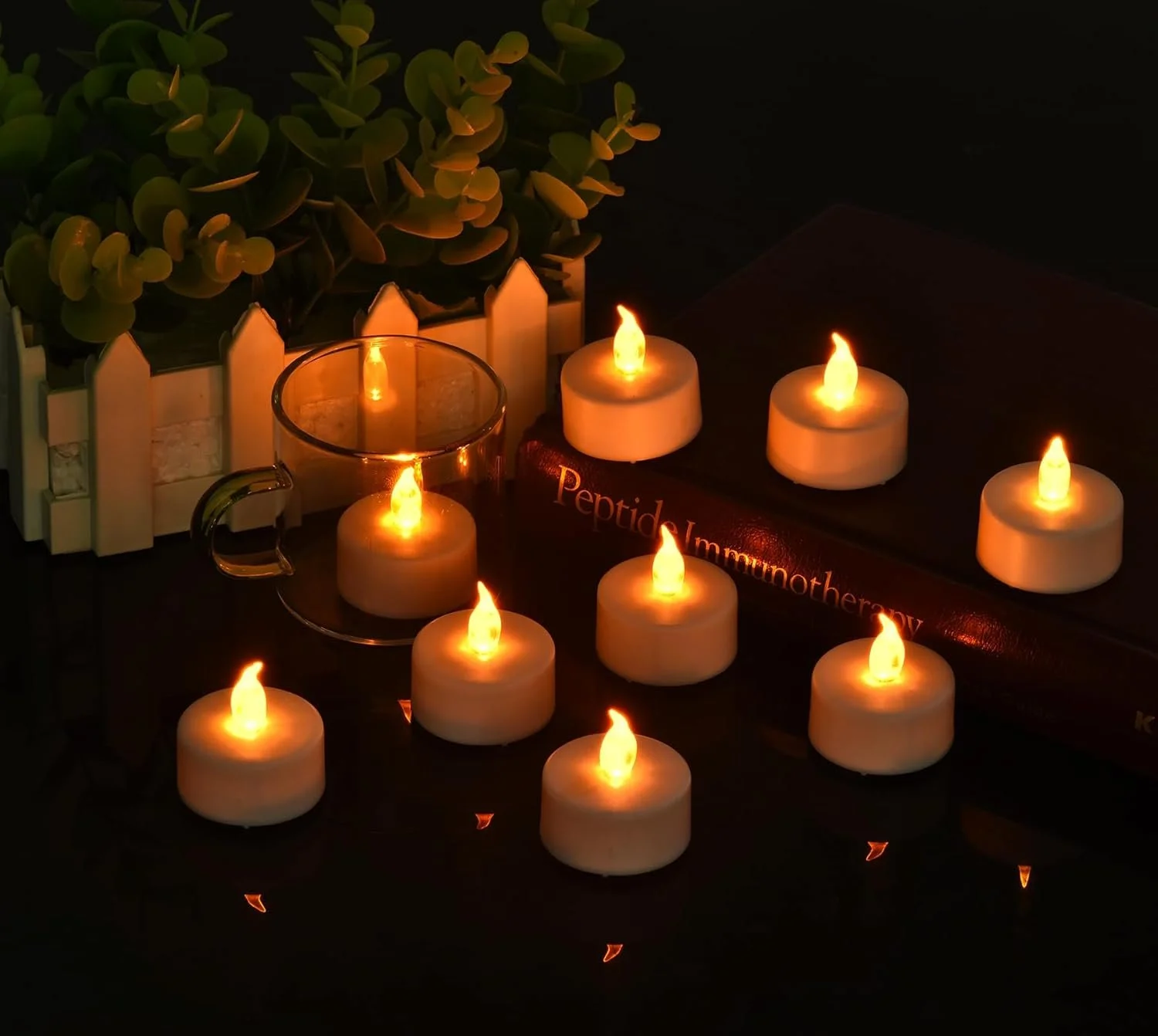 String text indicating the image shows multiple lit candles, a book titled 'Peptide Immunotherapy,' a glass cup with a small candle, and a potted plant on a dark surface.