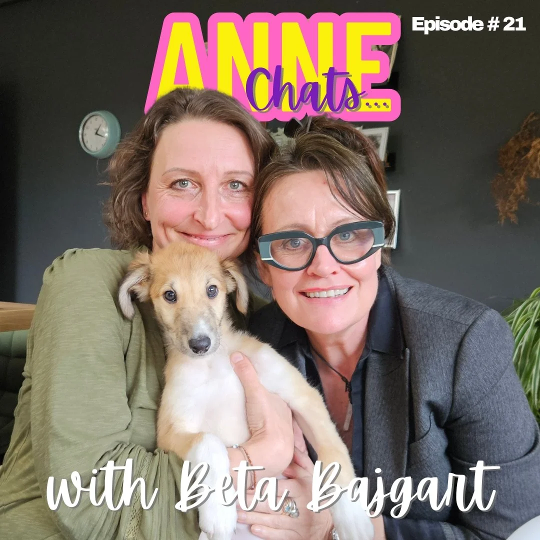 Two women smiling, one holding a puppy, against a black wall. Text overlays say 'AnneChats Episode #21' and 'with Beta Bagiart.'