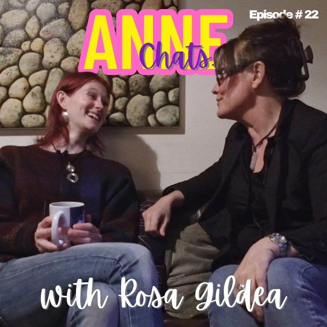 Two women sitting on a couch engaged in conversation, with a woman on the left holding a mug. There is a rock wall in the background and colorful text overlaying the image that reads "ANNE Chats" along with small text that says "Episode #22" and "with Rosa Gildea."