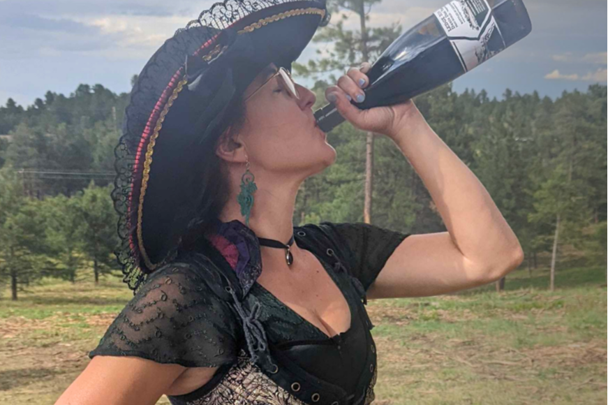 A woman in a pirate costume taking a swig from a wine bottle at the Renaissance festival
