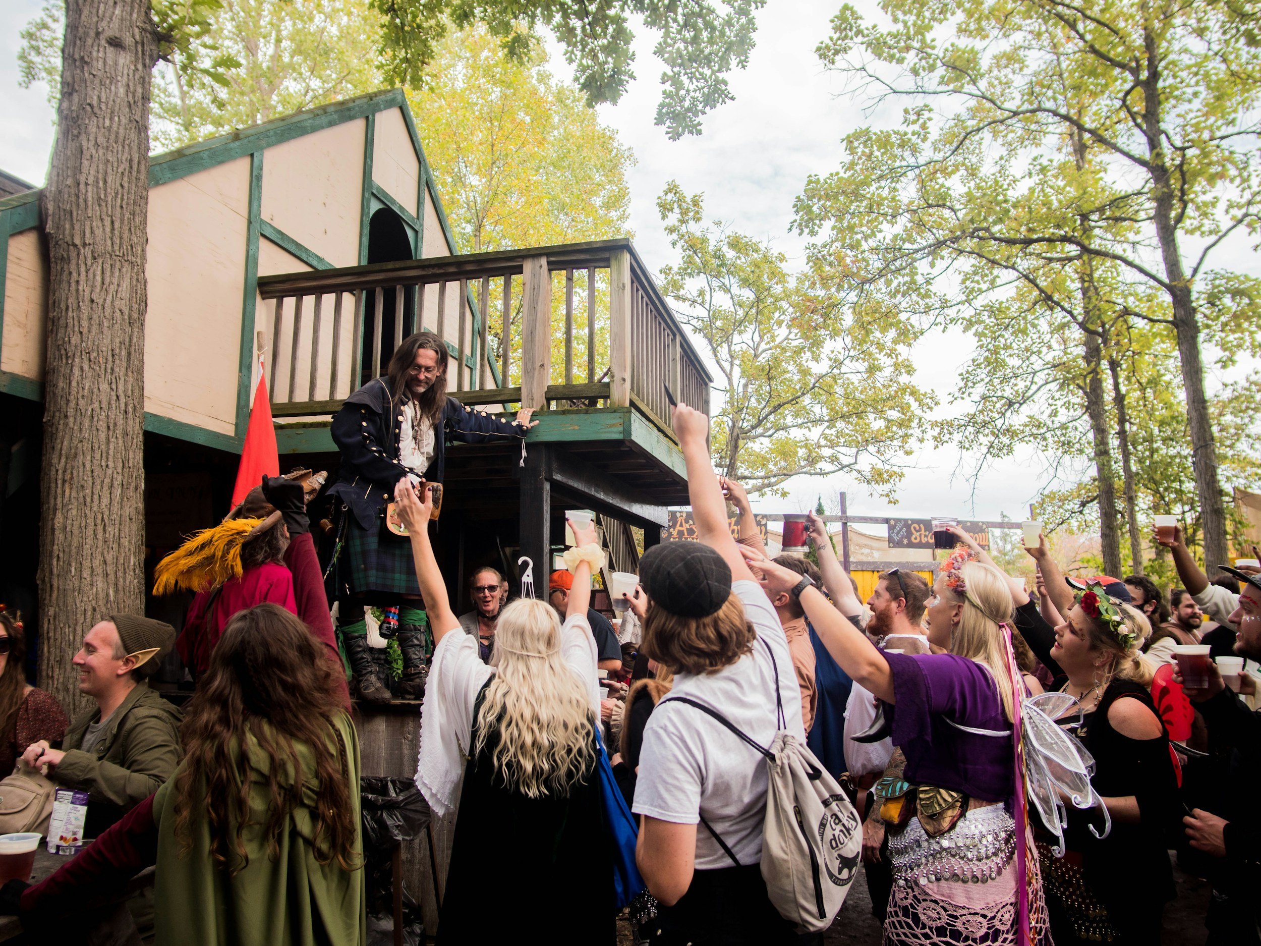 a crowd gathered at a renaissance festival, cheering with their hands raised