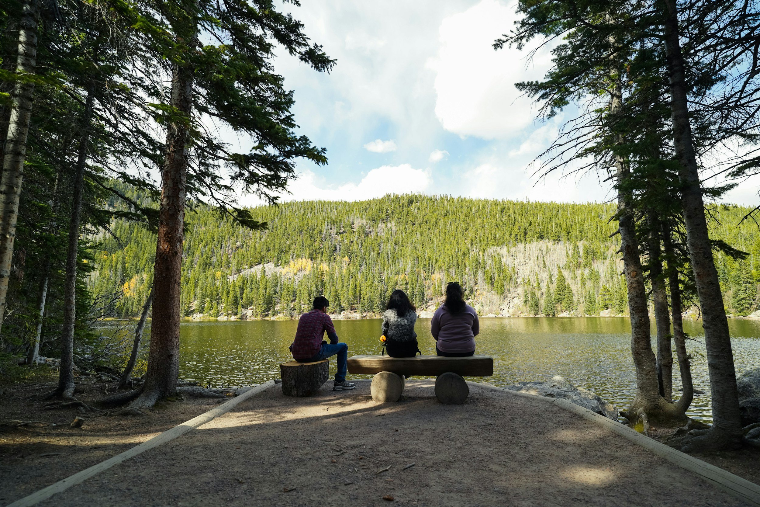 three people sitting on logs and facing a scenic lake