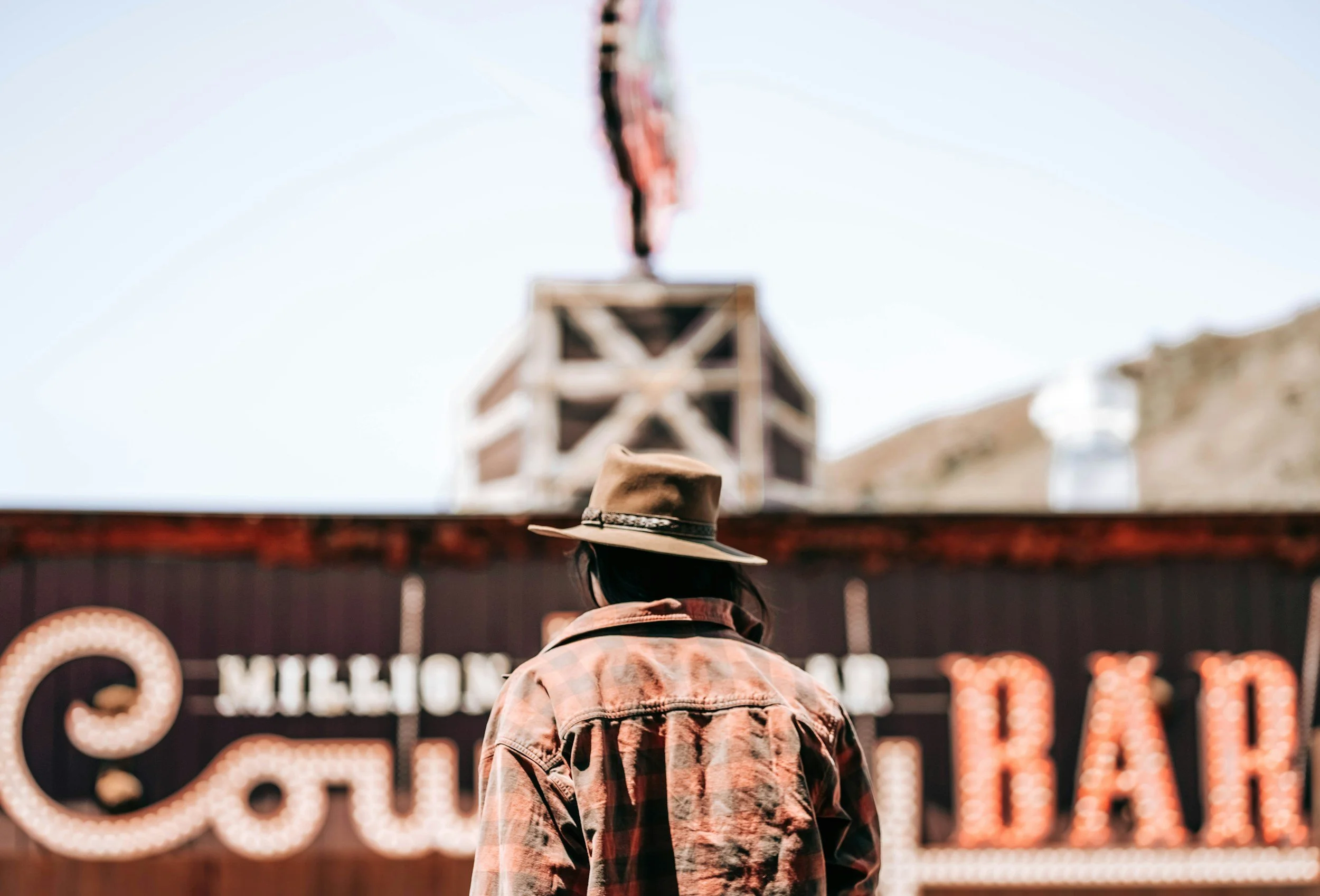 cowboy facing away from the camera with a blurred rodeo background