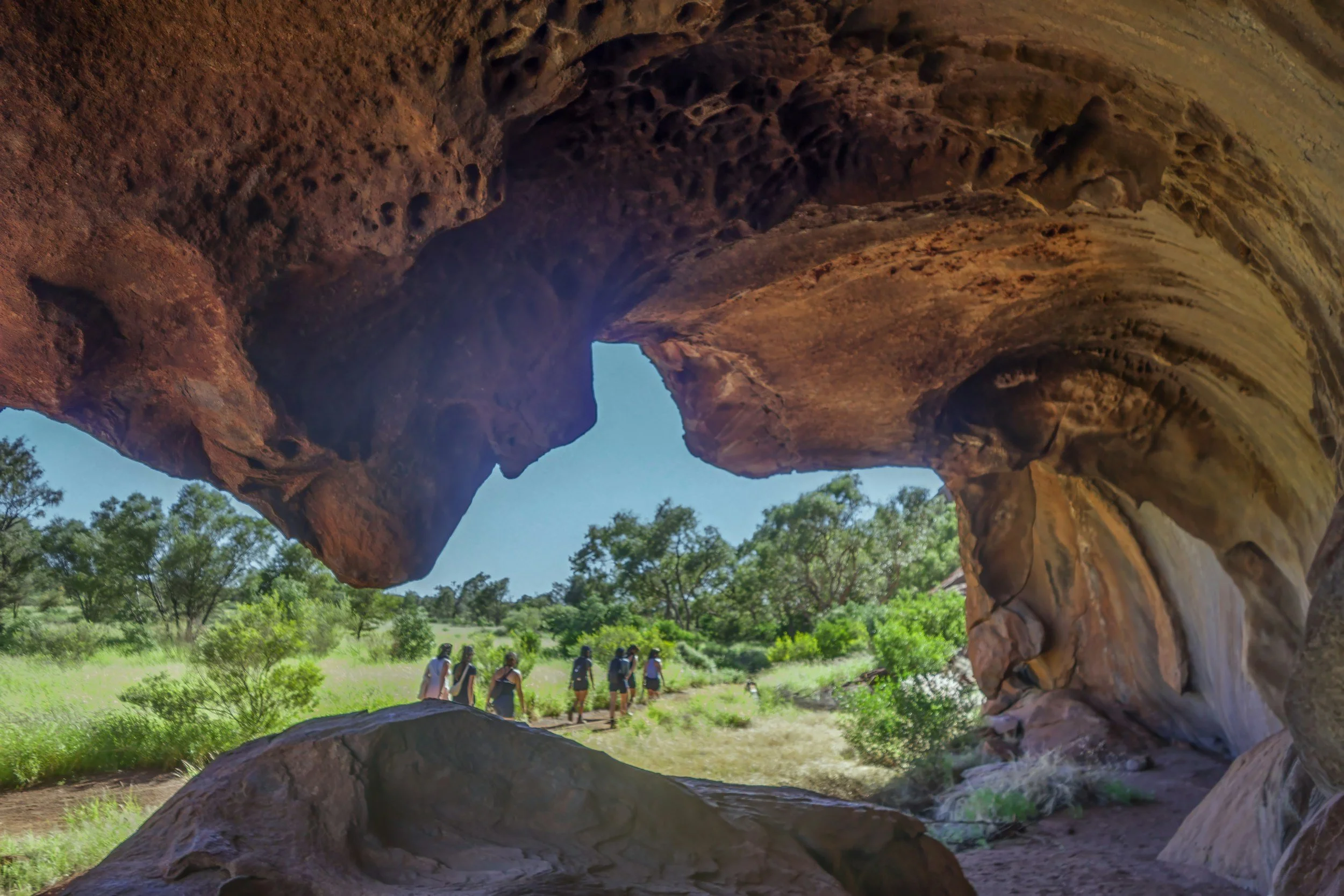 a group of hikers walking on a trail path, seen through the viewpoint of being inside a cave