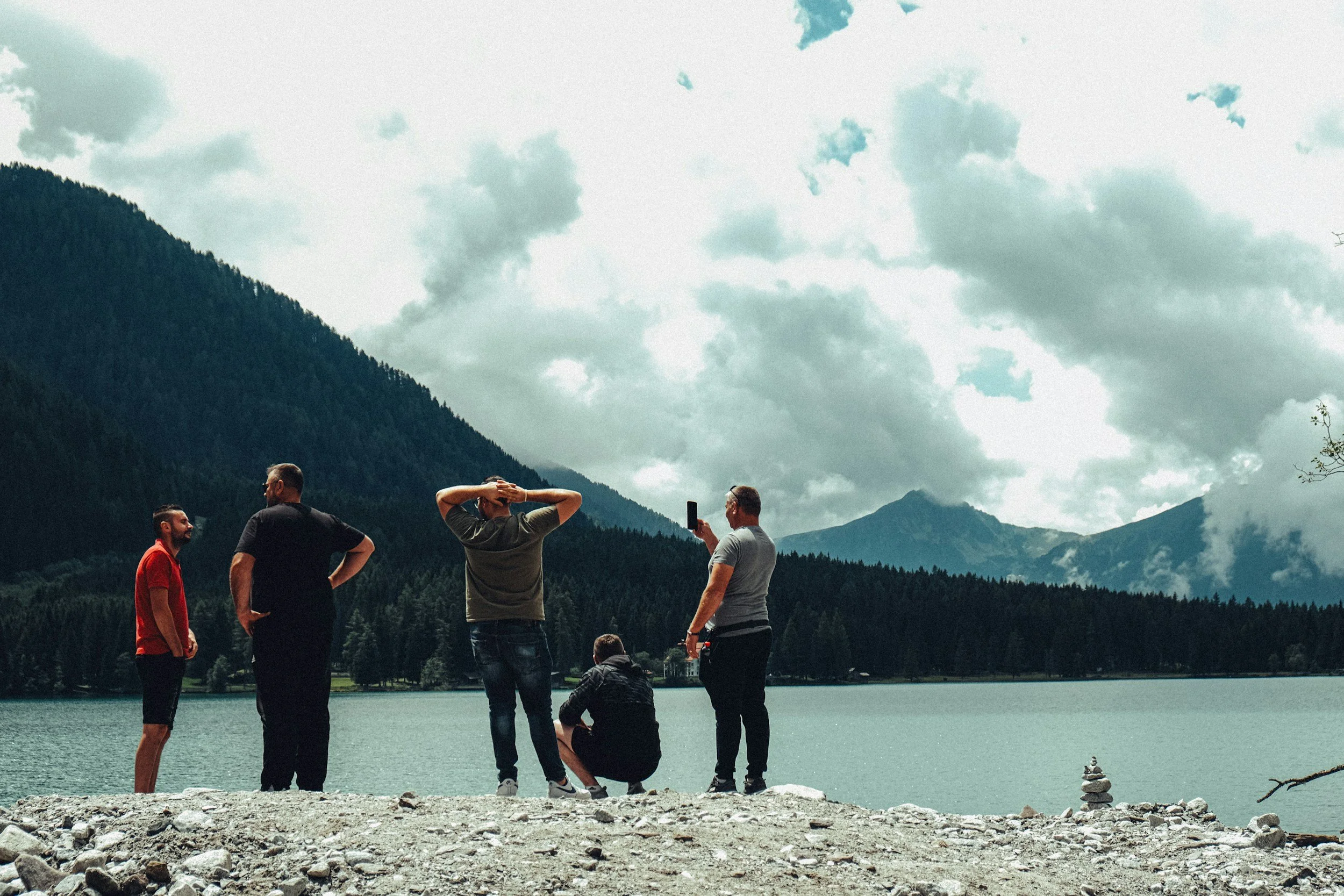 a group standing beside a lake with a mountainous forest in the background