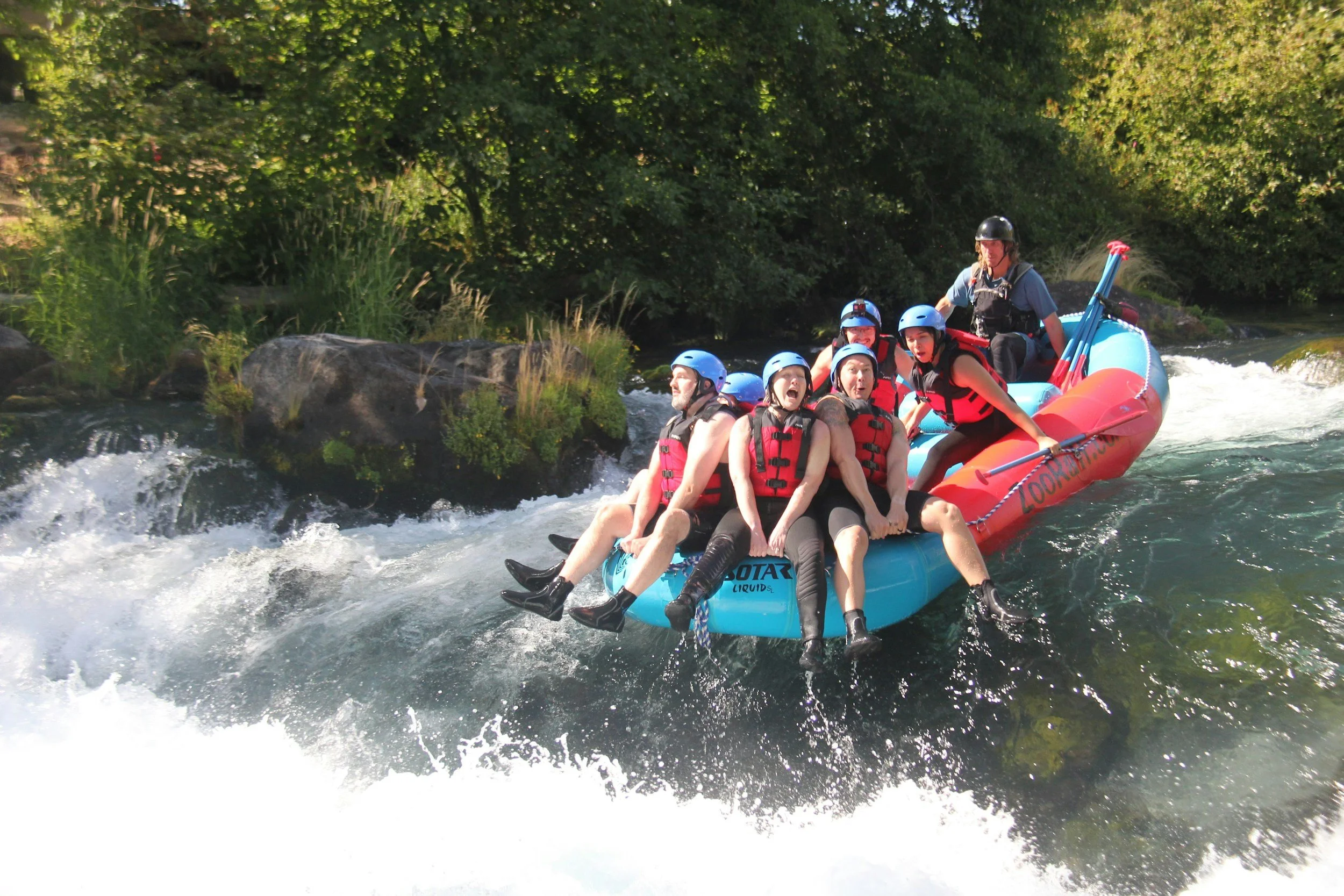 a group of white water rafters having fun straddling the edge of their raft as they go over some rapids