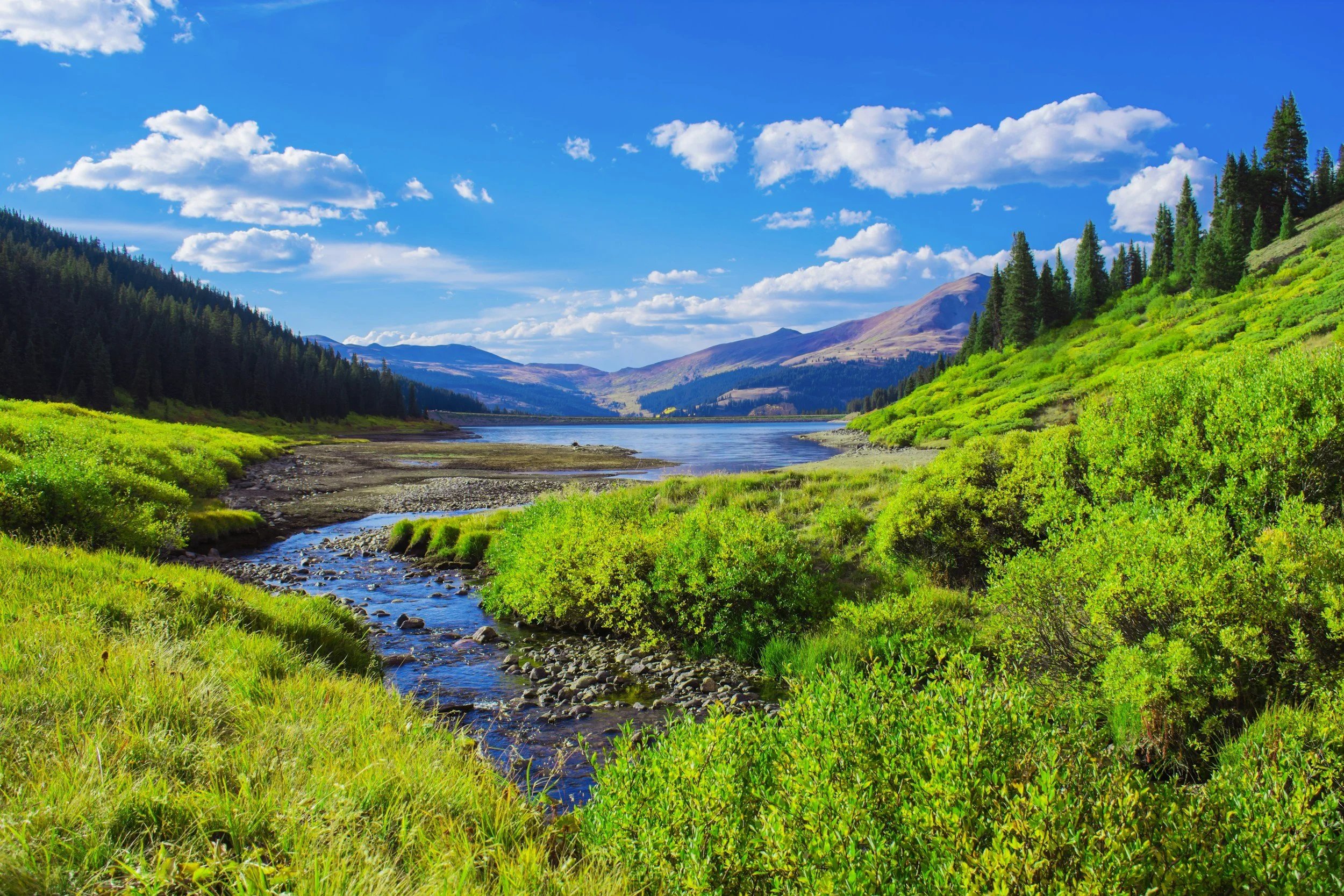 a beautiful scenic landscape photo of Breckenridge where you can see a grassy knoll with a lake in the background and mountains in the distance