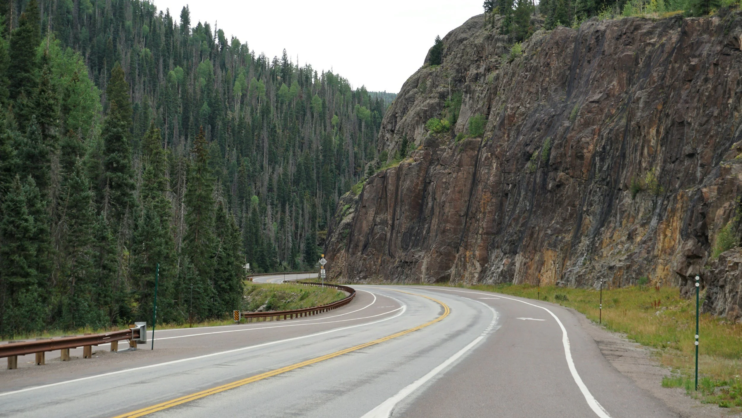 a winding road curves to continue past a mountainous forest