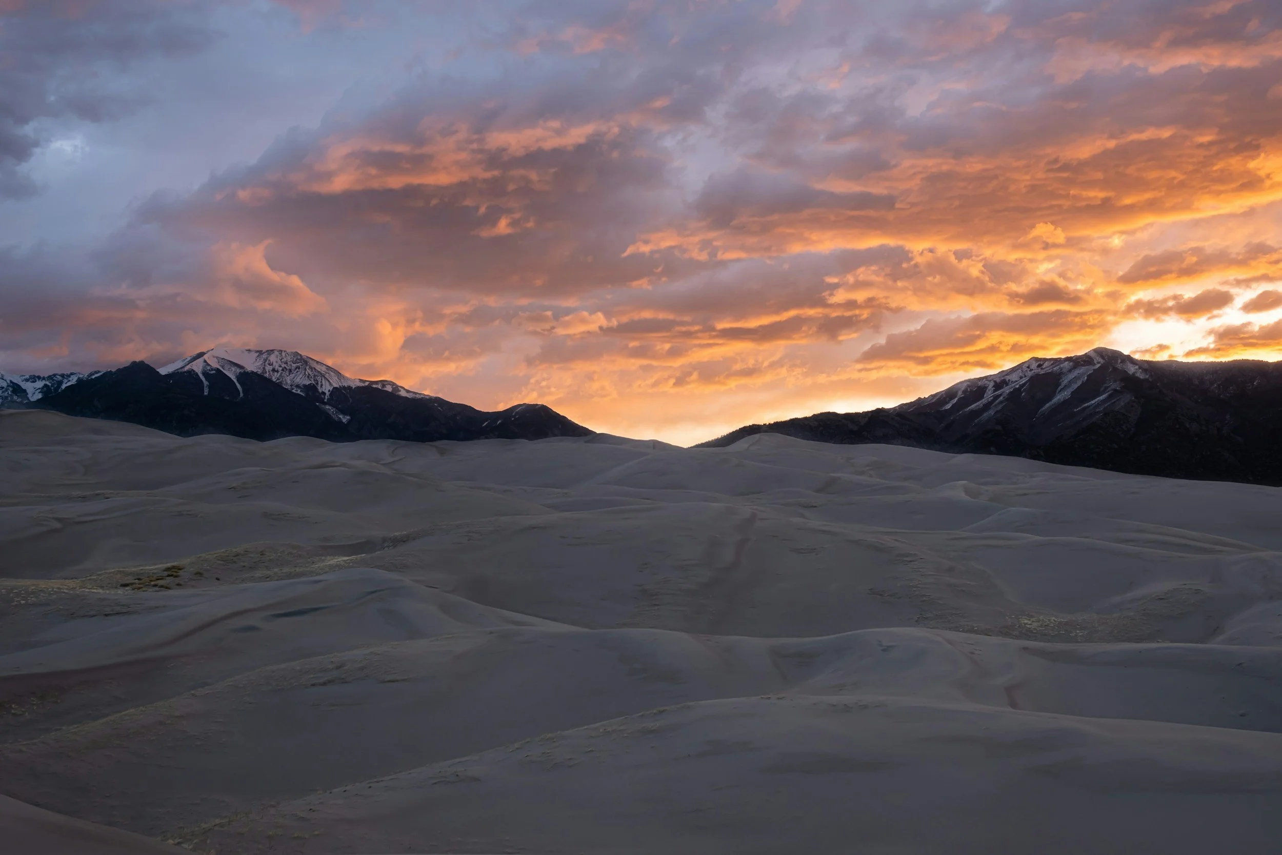 Great sand dunes with a mountain landscape in the background and a setting sun in the distance