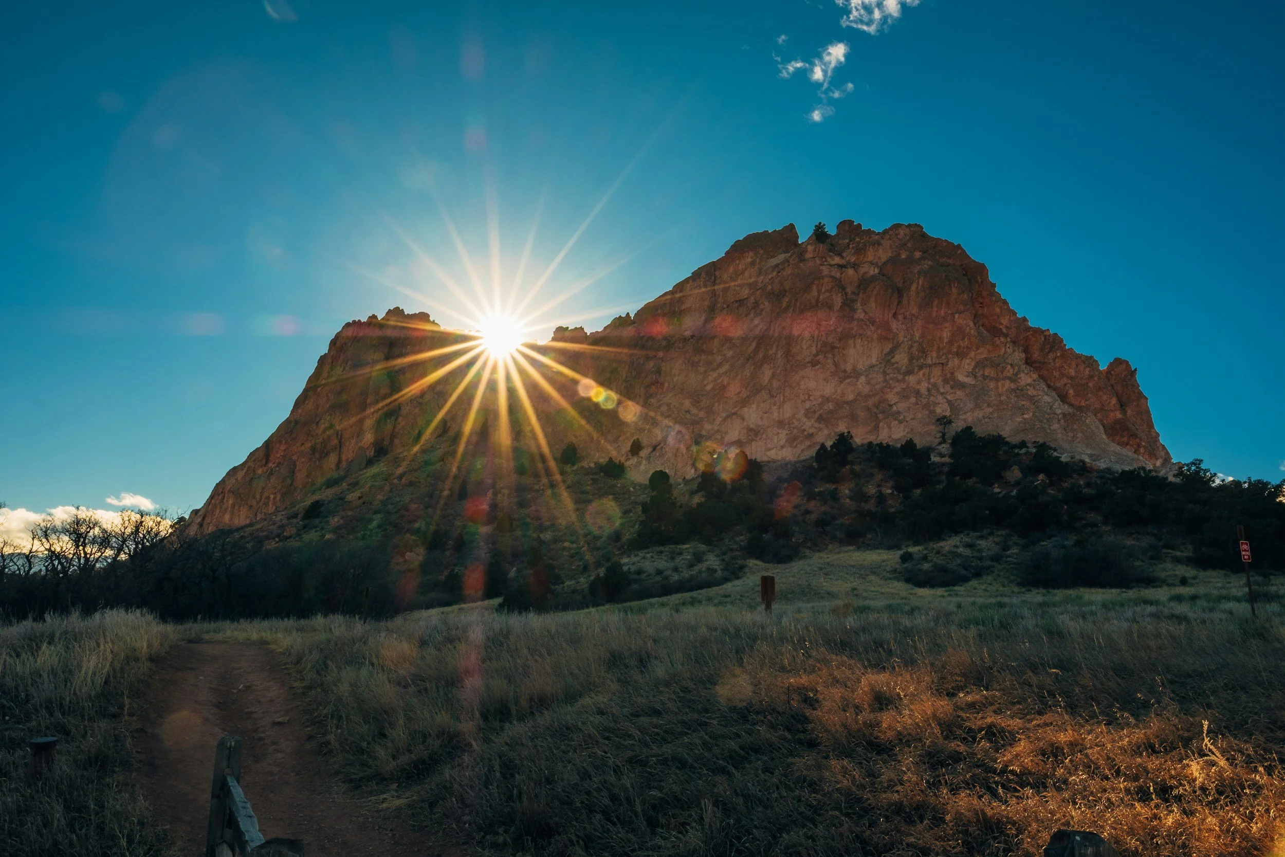 a sunburst visible cresting the top of a mountain peak at garden of the gods