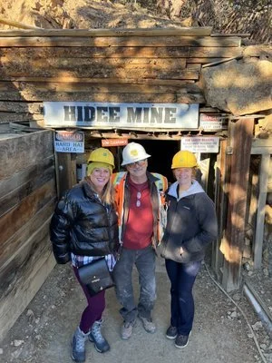 Three people in hard hats stand in front of the entrance of Hidee Mine