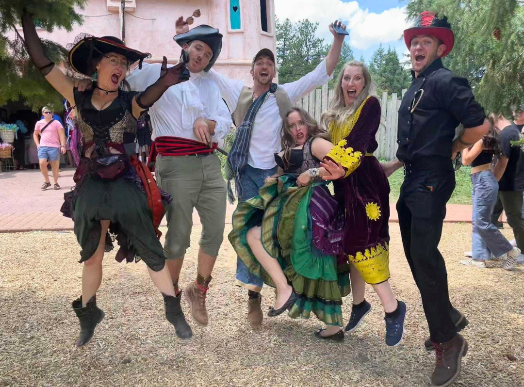 A group of friends jumping for joy while wearing costumes at a Renaissance Festival