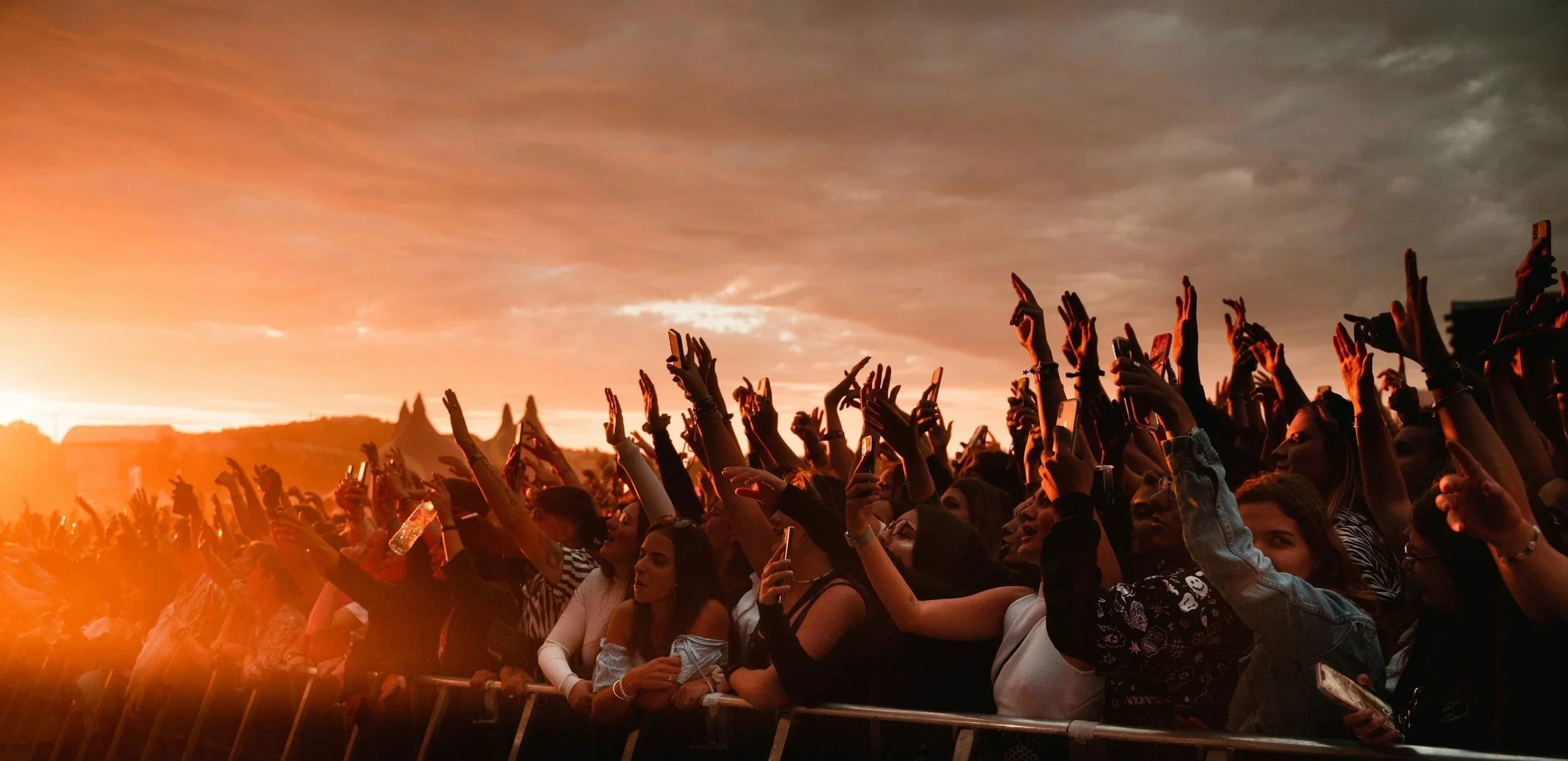 A crowd at Red Rocks amphitheater raising up their hands at sunset
