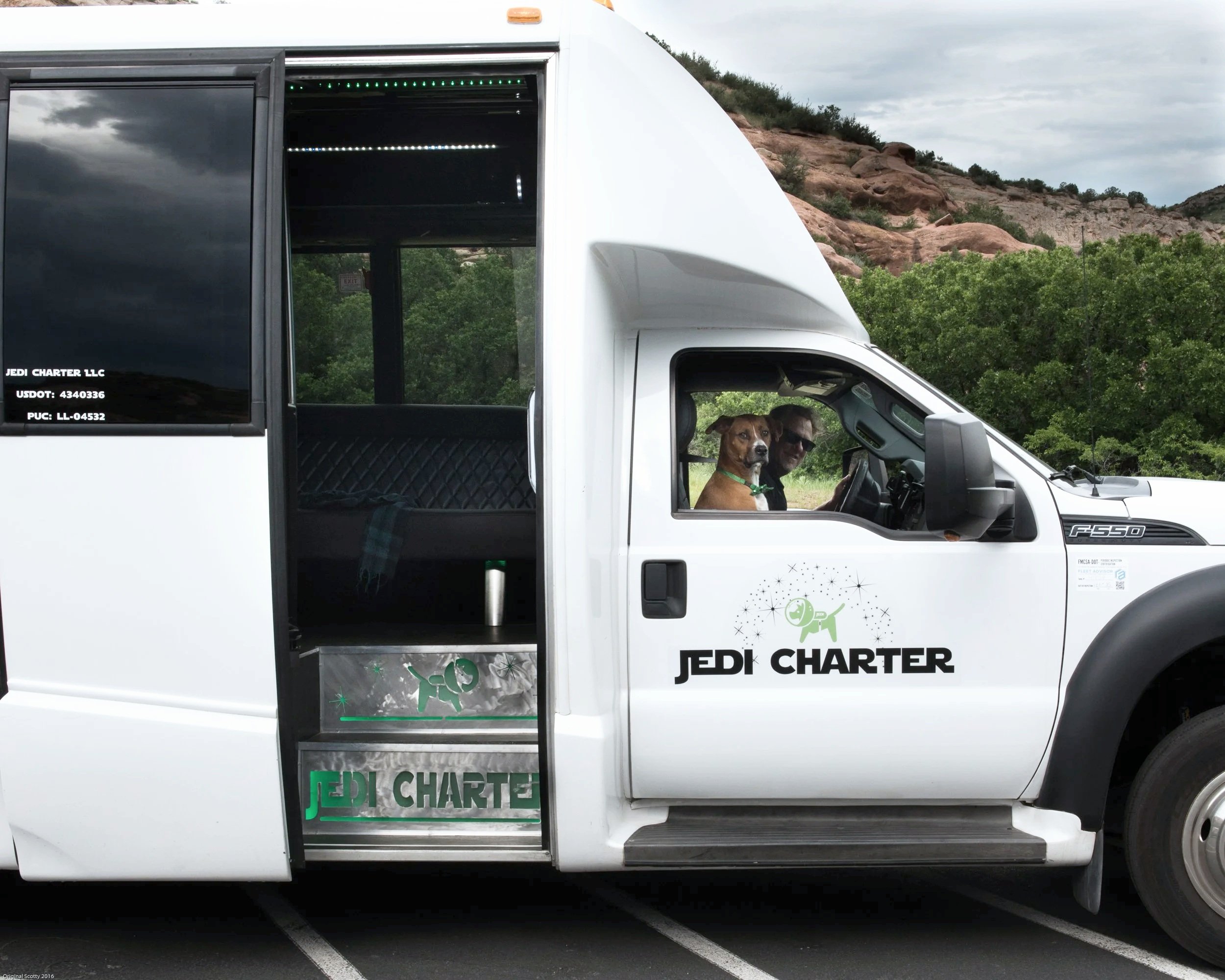 A dog sits in the front seat with the driver of the Jedi Charter bus