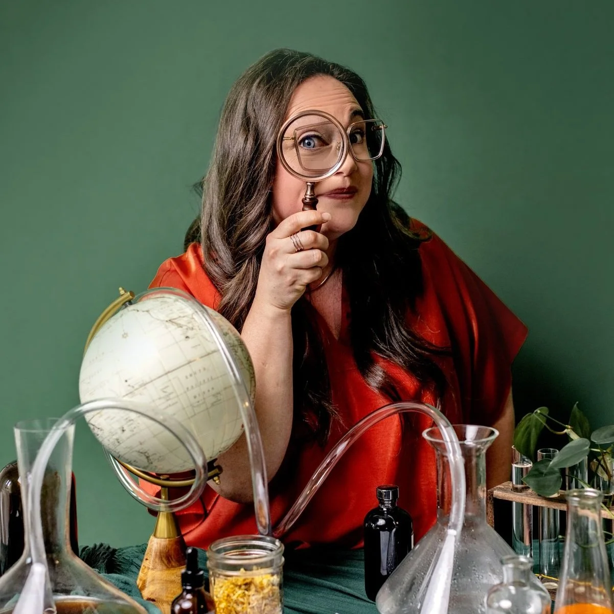 Woman with magnifying glass, globe, and laboratory equipment on table.