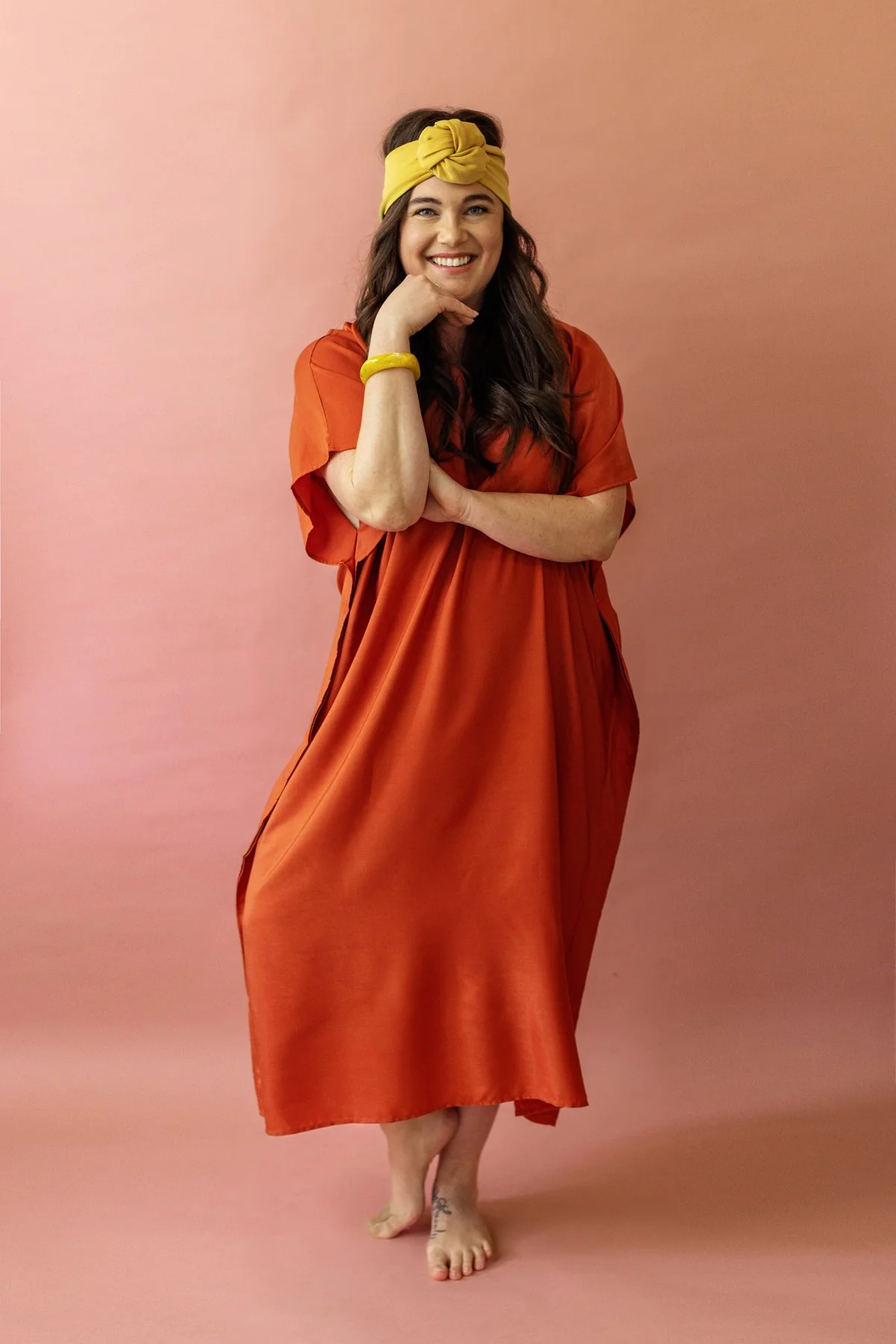 Woman wearing an orange dress and yellow headband against a pink background.