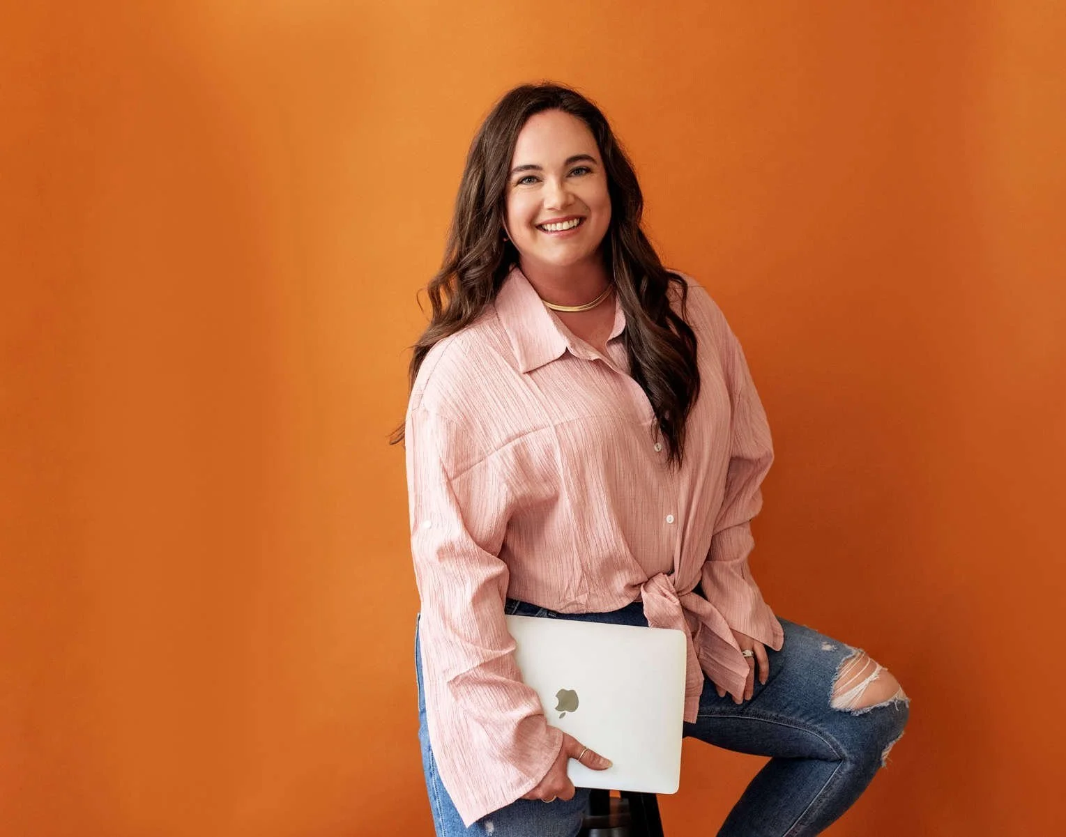 Woman in pink shirt holding a laptop against an orange background