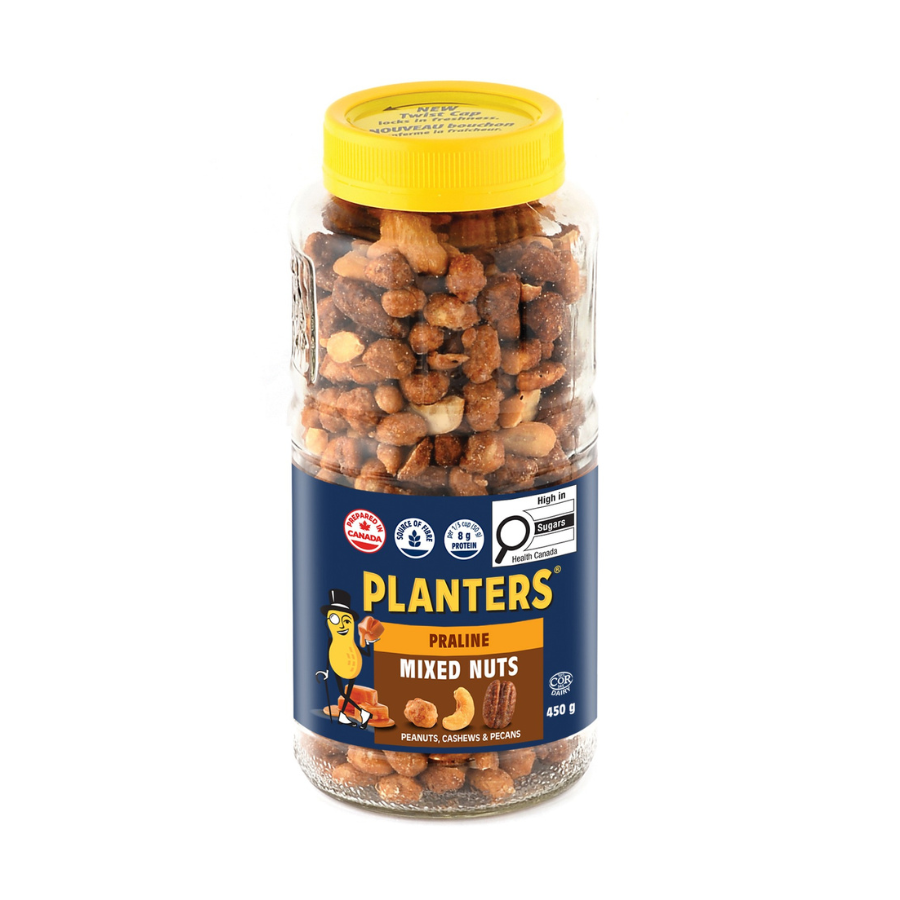 A clear glass jar of Planters Praline Mixed Nuts with a yellow lid and label featuring a cartoon peanut character, product details, and nutrition facts.