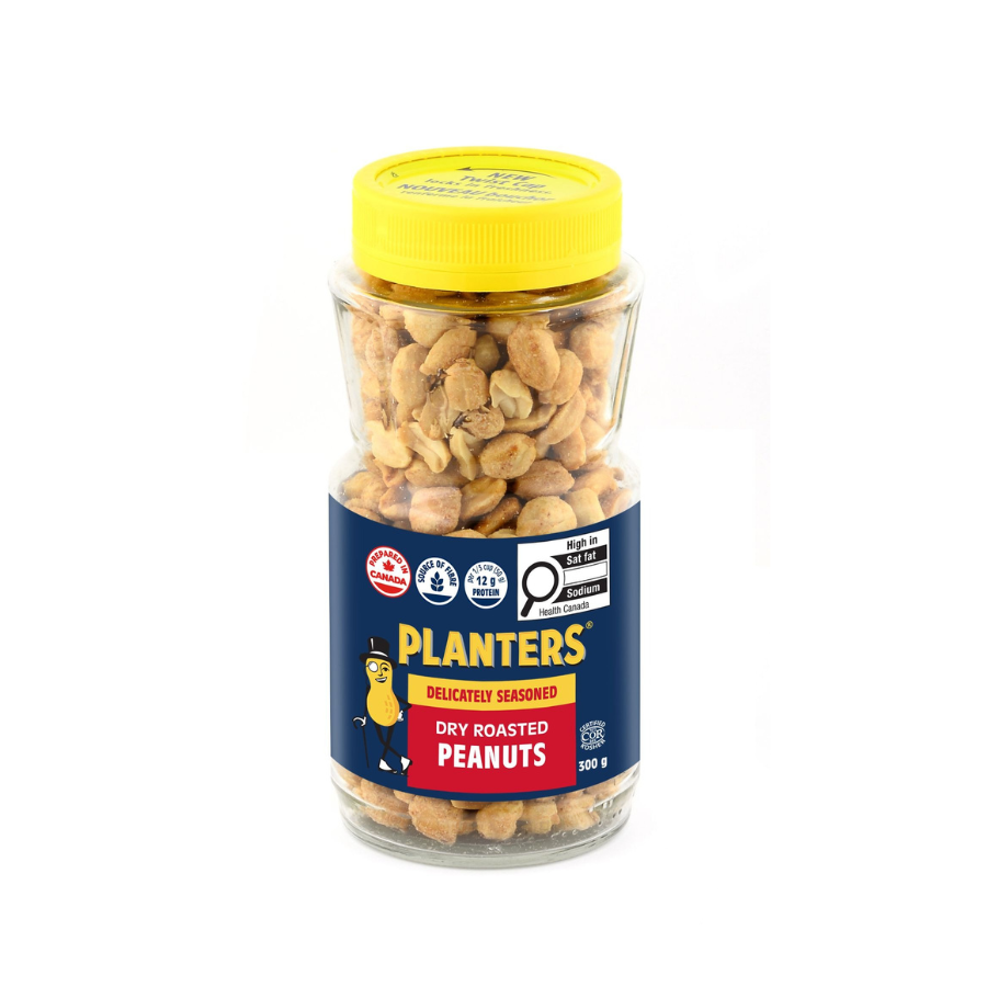 A clear glass jar with a yellow lid holding dry roasted peanuts, labeled 'Planters Delicately Seasoned Dry Roasted Peanuts'.