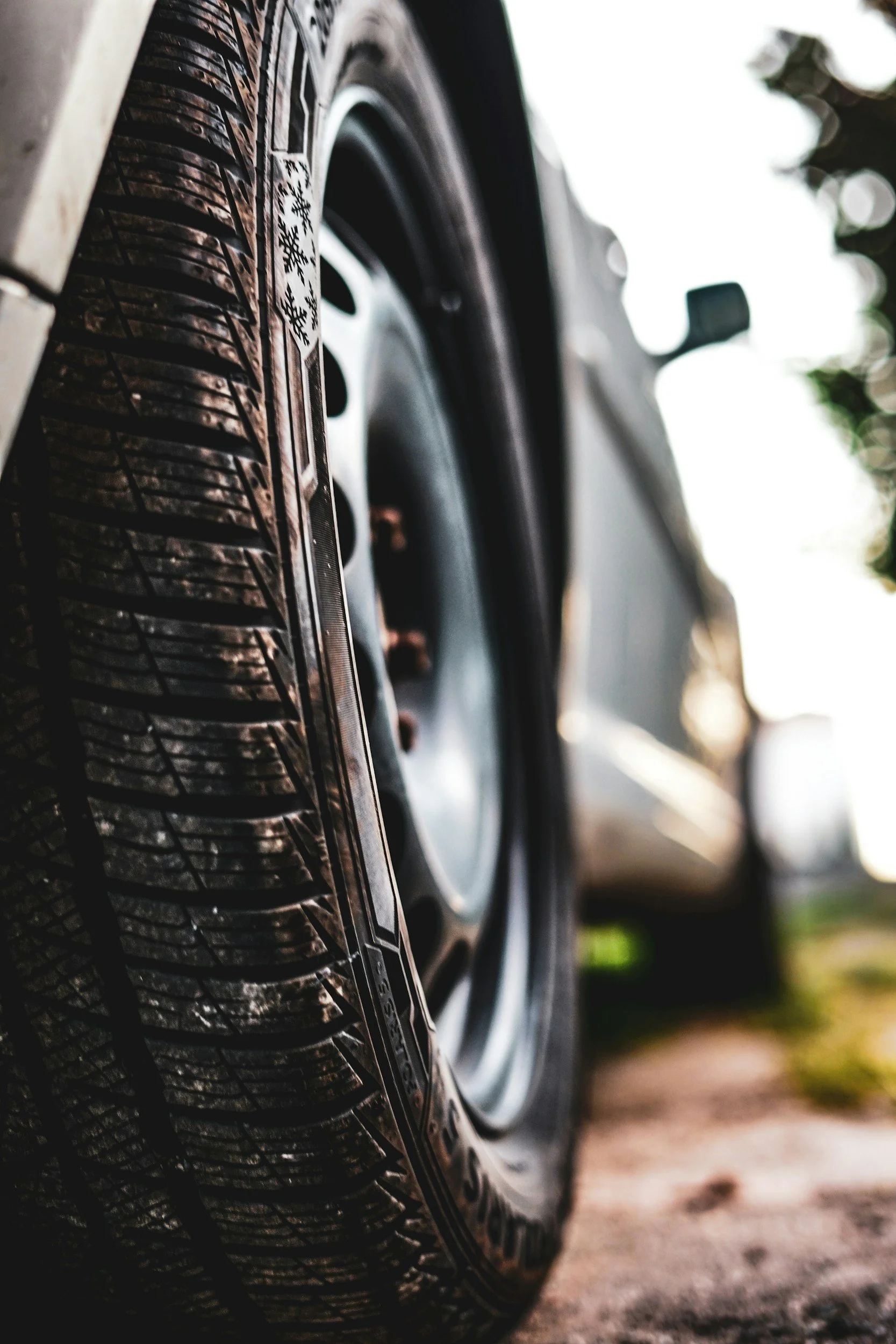 Close-up of a car tire on a vehicle parked outdoors with trees and sky in the background.