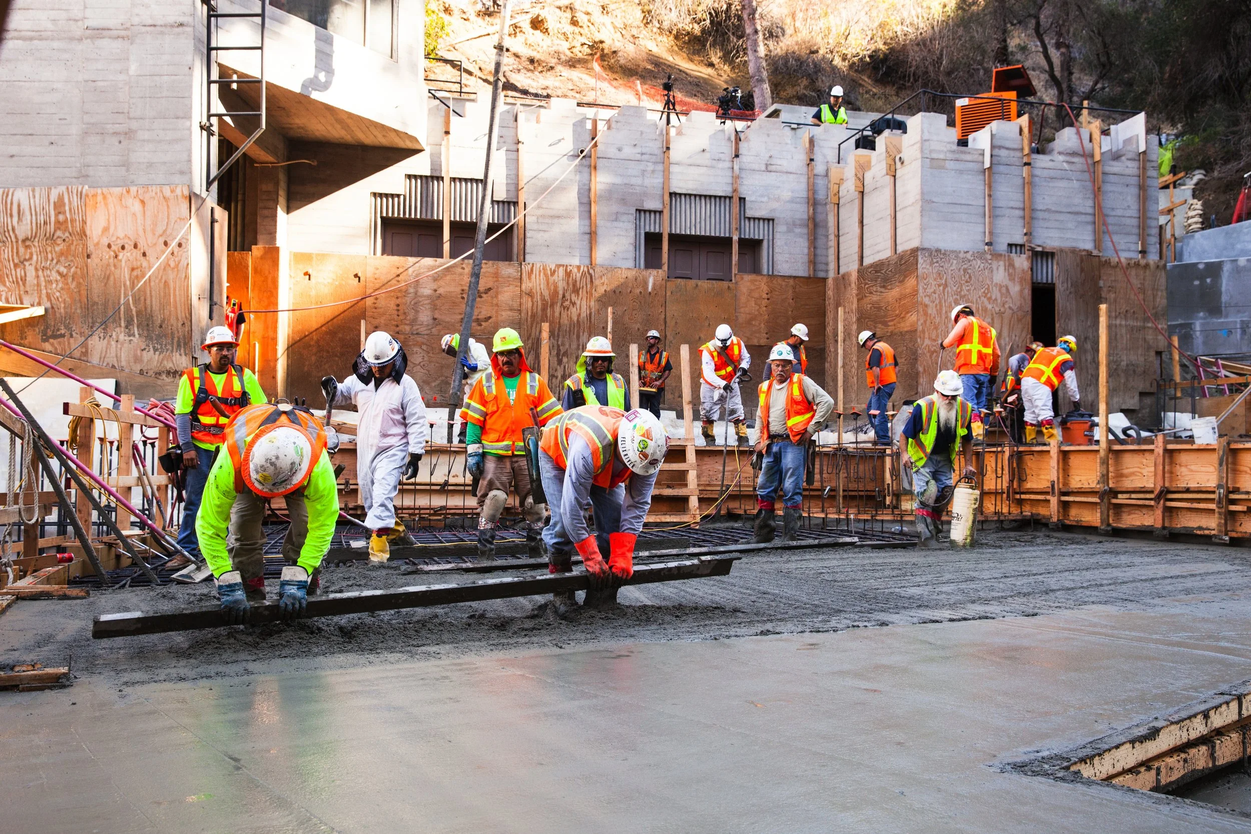 Construction workers wearing safety gear and vests pouring and leveling concrete on a building site.